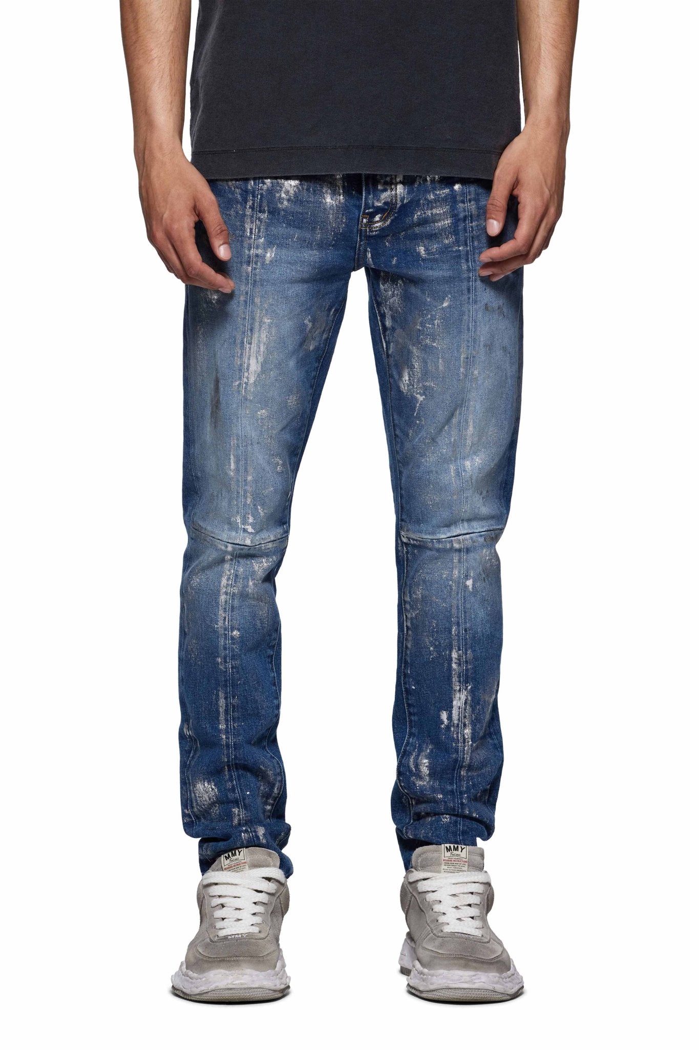 A person in a black shirt and PURPLE BRAND's Purple Brand P001-SAFC Angel Silver Foil Cross Indigo jeans, paired with light gray sneakers, stands against a white background.