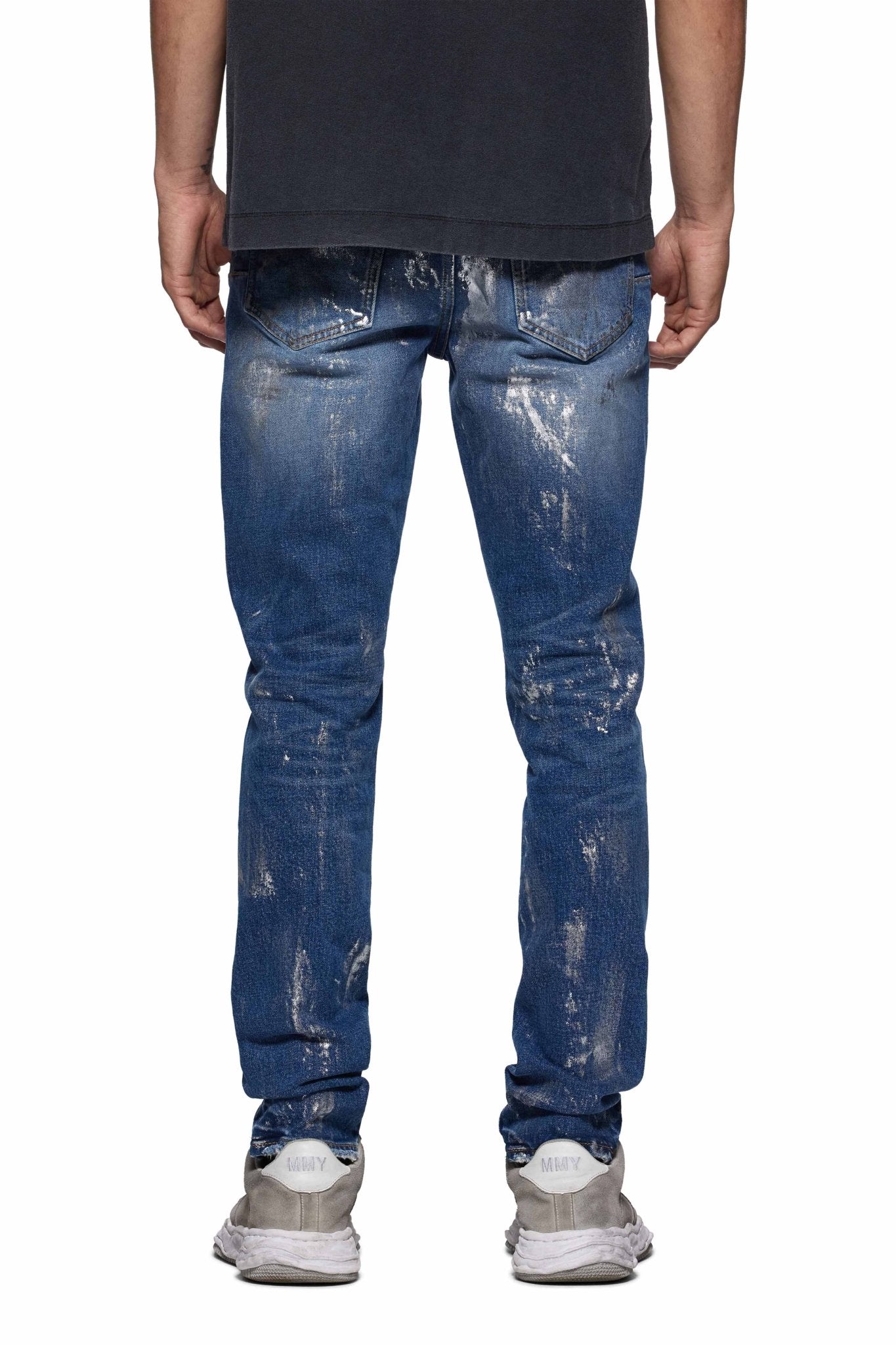 The person is wearing a black shirt, PURPLE BRAND's premium stretch denim P001-SAFC Angel Silver Foil Cross Indigo jeans, and white sneakers, viewed from the back.