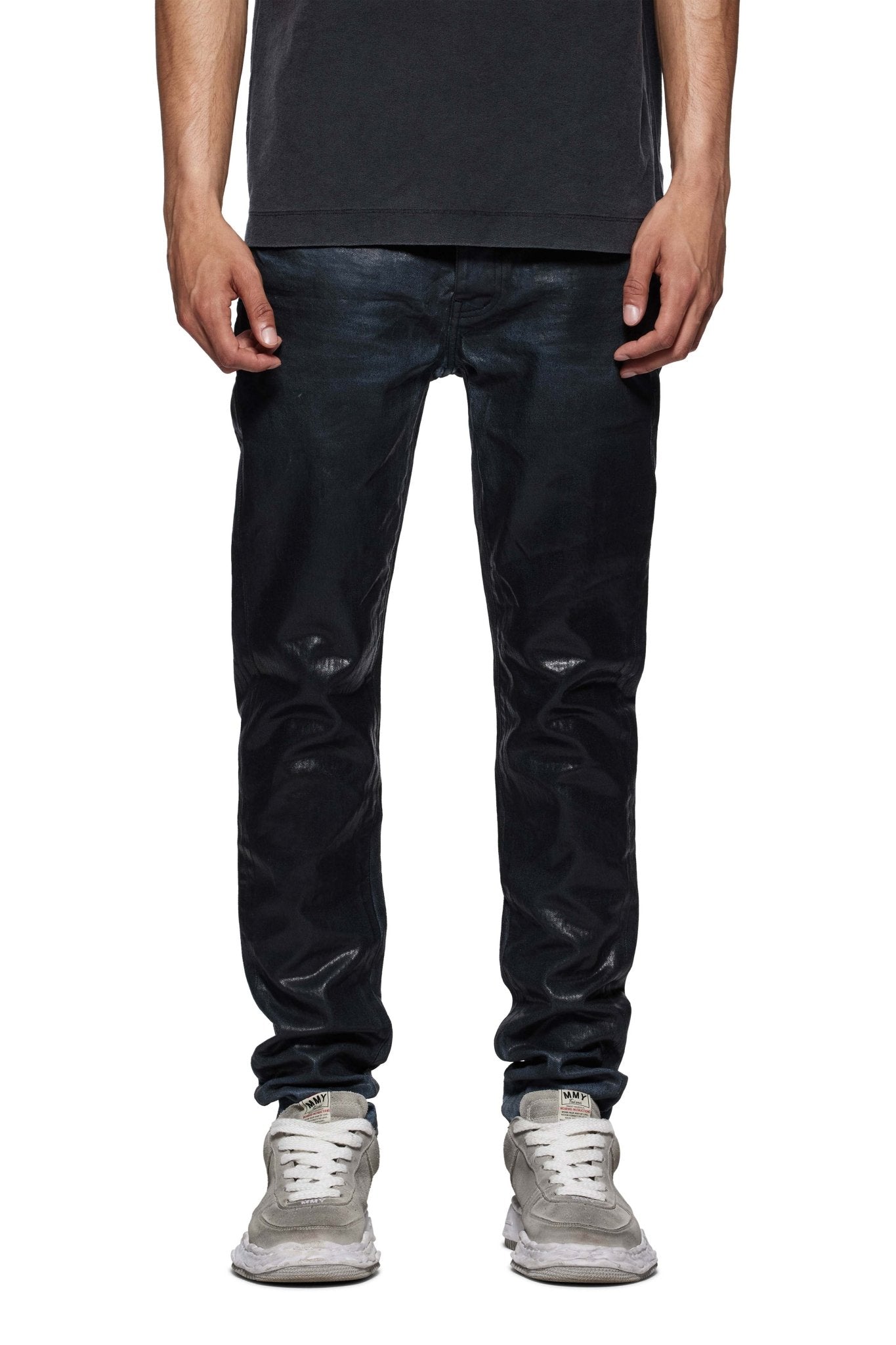 A person wearing PURPLE BRAND's P001-SCBI Skinny Black Coated Indigo jeans, a black shirt, and gray sneakers stands against a white background.