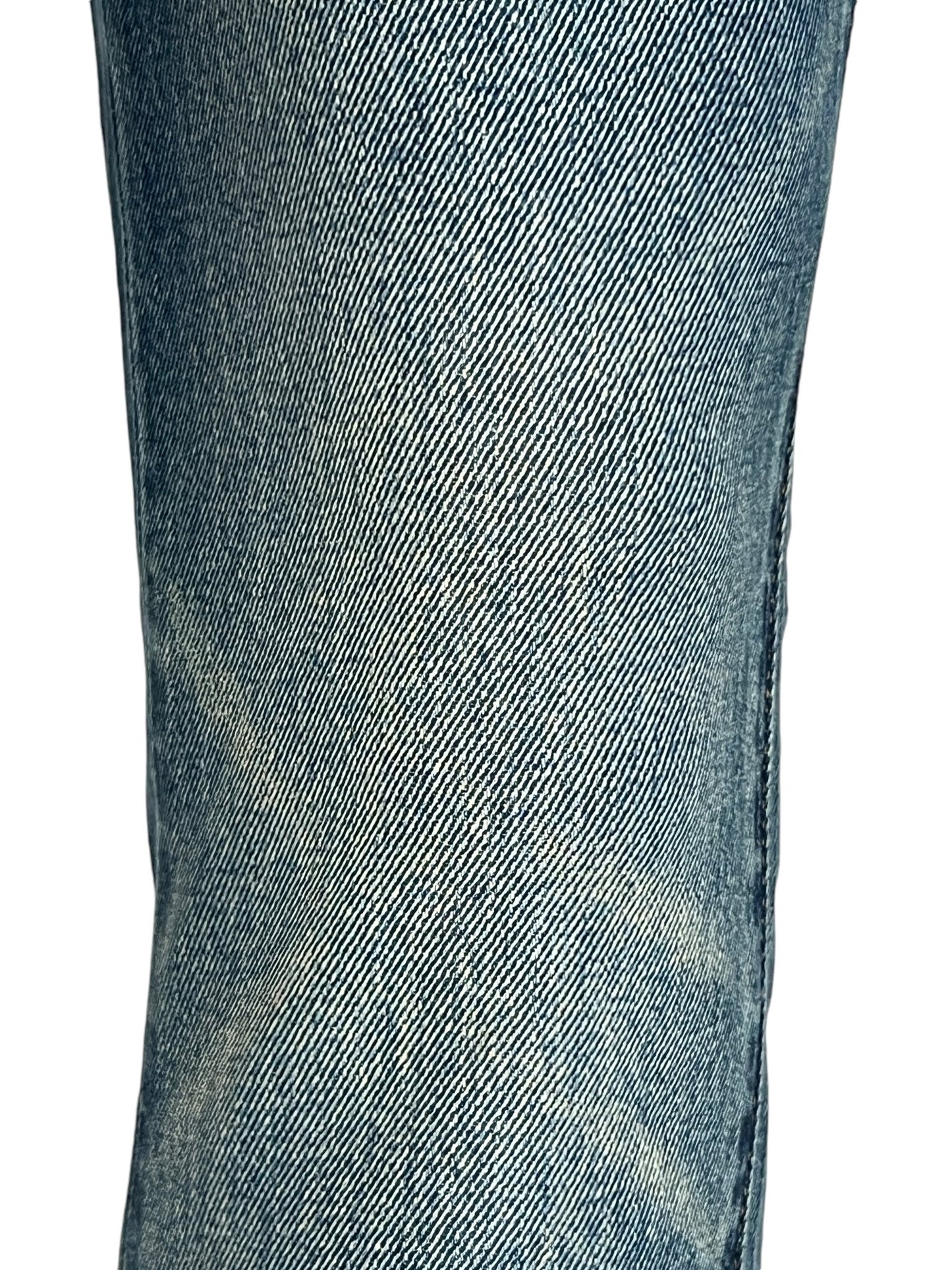 Close-up of a person's leg wearing faded blue PURPLE BRAND P001-SDTE SKINNY COATED DK TEMPEST DK INDIGO jeans, showcasing the texture and weave of the skinny fit fabric.