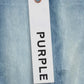 A white tag with "PURPLE BRAND" in black letters hangs by a copper ball chain against the light indigo backdrop of premium stretch denim from the Purple Brand P001-SKCI Skinny Coated collection.