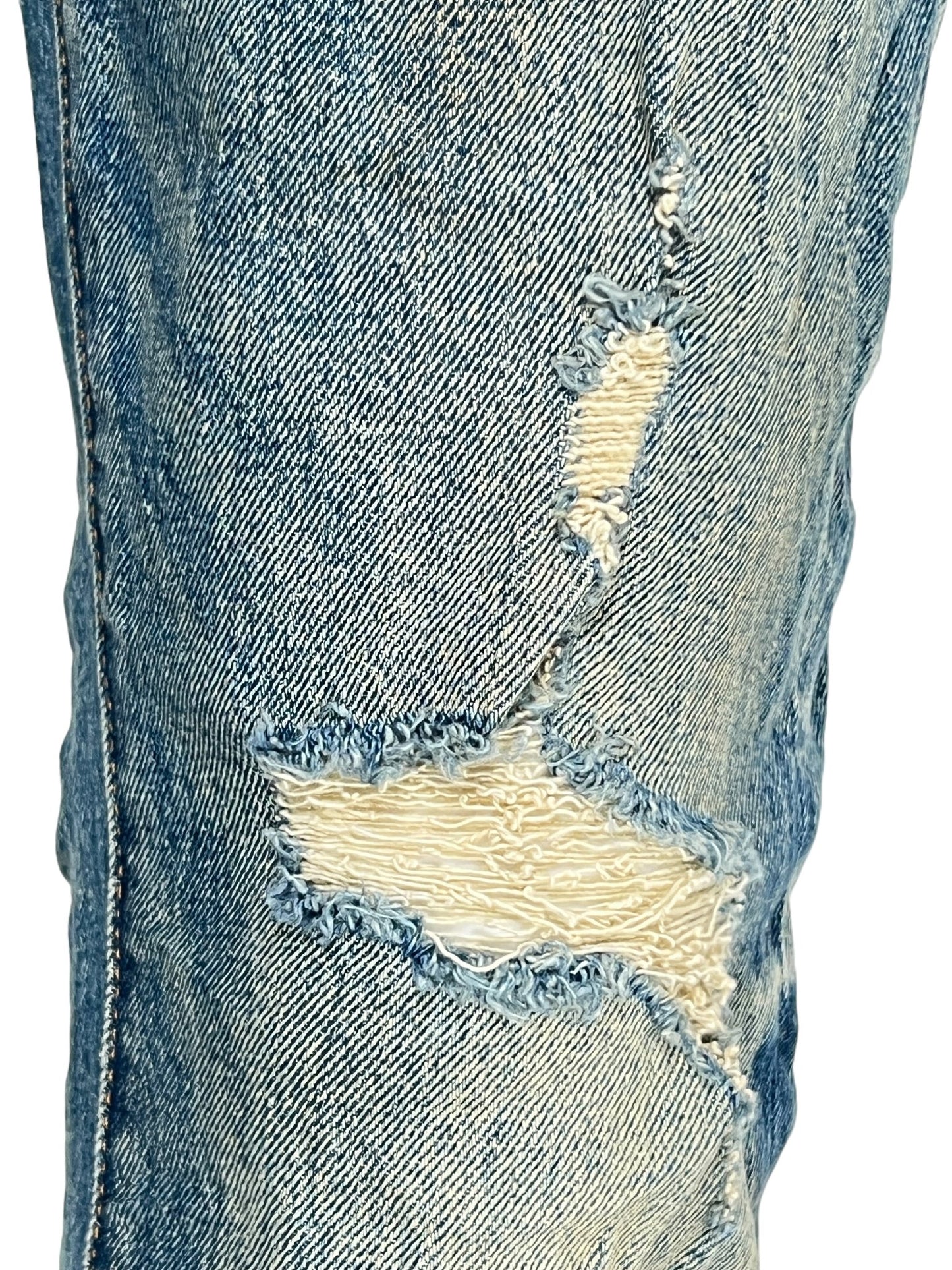 Close-up of a pair of PURPLE BRAND P001-SNFD SKINNY 9 TO 5 DK INDIGO jeans with distressed detailing, featuring two large frayed holes, one on the thigh and one on the knee. Crafted from premium stretch denim, these standout jeans are perfect for Fall Winter 2024.