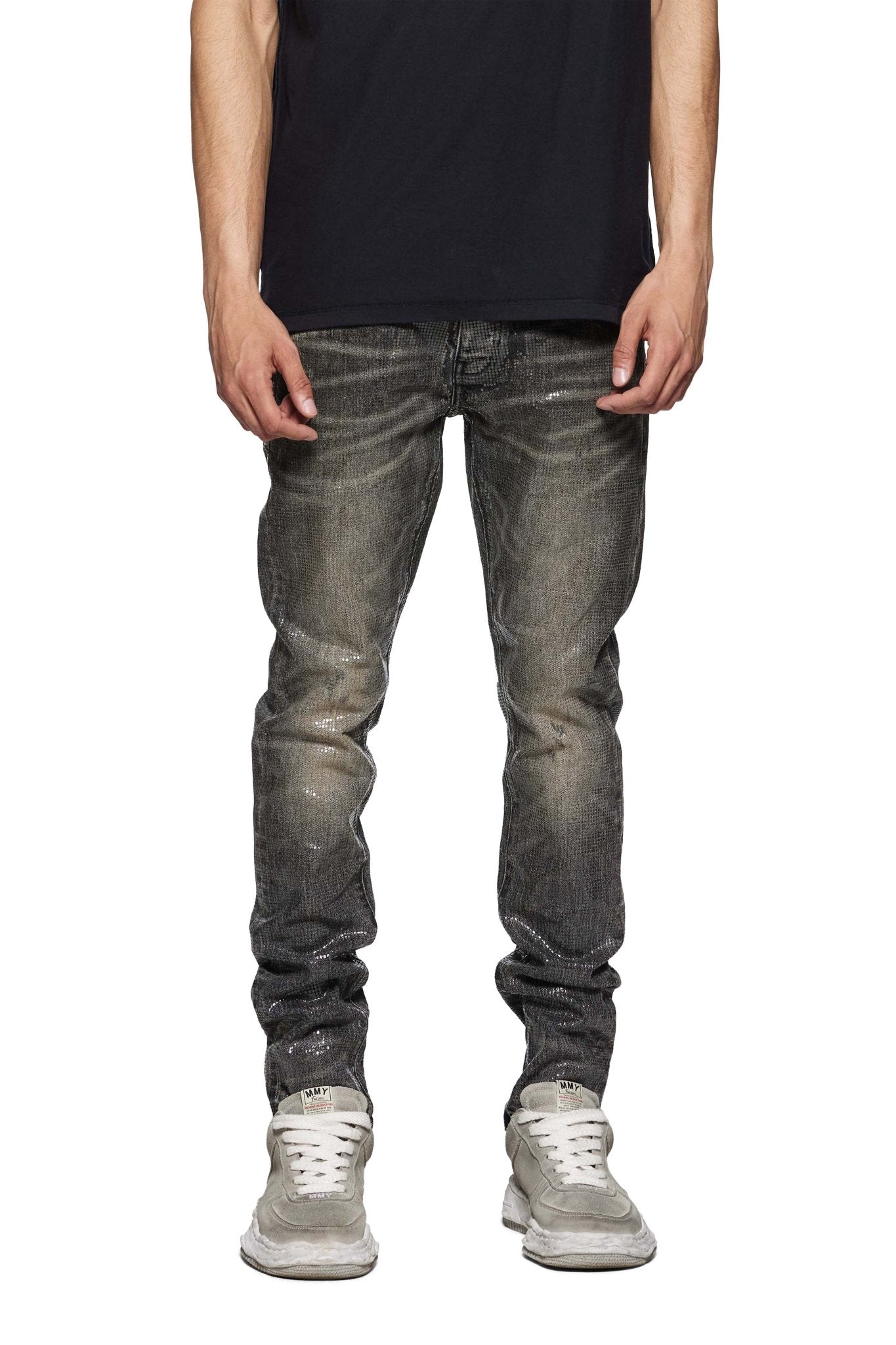 A person wearing a Purple Brand P001-TOBL Tiled Overlay Black shirt, distressed gray low-rise skinny jeans made of premium stretch denim, and white sneakers stands against a plain white background.