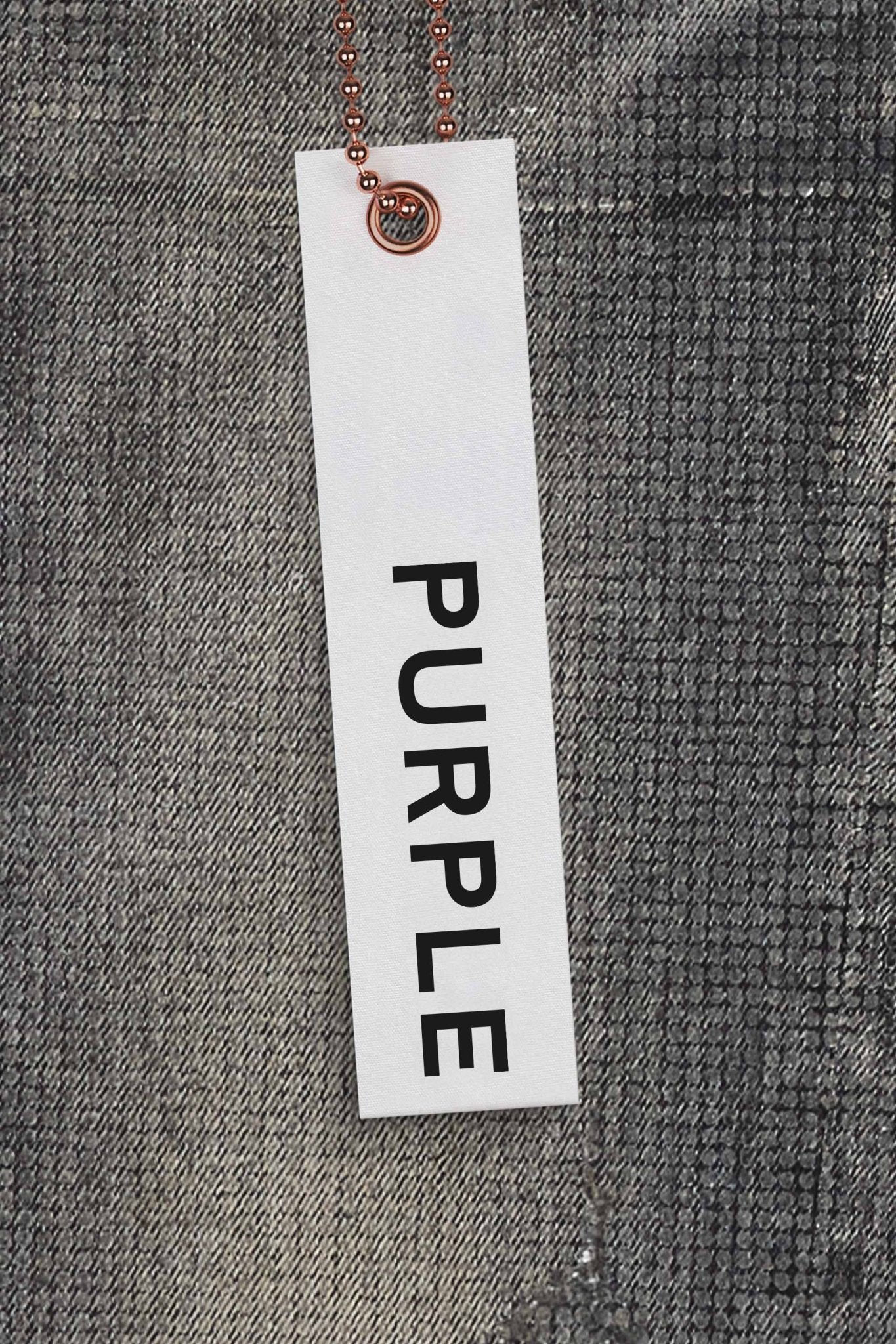 Against a textured gray fabric, a white tag with "PURPLE BRAND" in bold black letters pops, recalling the look of premium stretch denim associated with the Purple Brand P001-TOBL Tiled Overlay Black.
