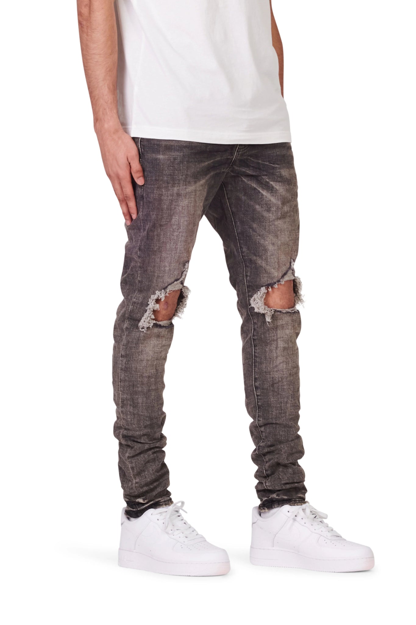 A person wearing a white t-shirt, white sneakers, and PURPLE BRAND Purple Brand P002-VWBO Vintage Worn Blowout Black distressed jeans stands against a plain background.