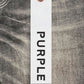 A white tag with "PURPLE" in black hangs by a chain against a pair of PURPLE BRAND P002-VWBO Vintage Worn Blowout Black jeans, crafted from premium stretch denim.