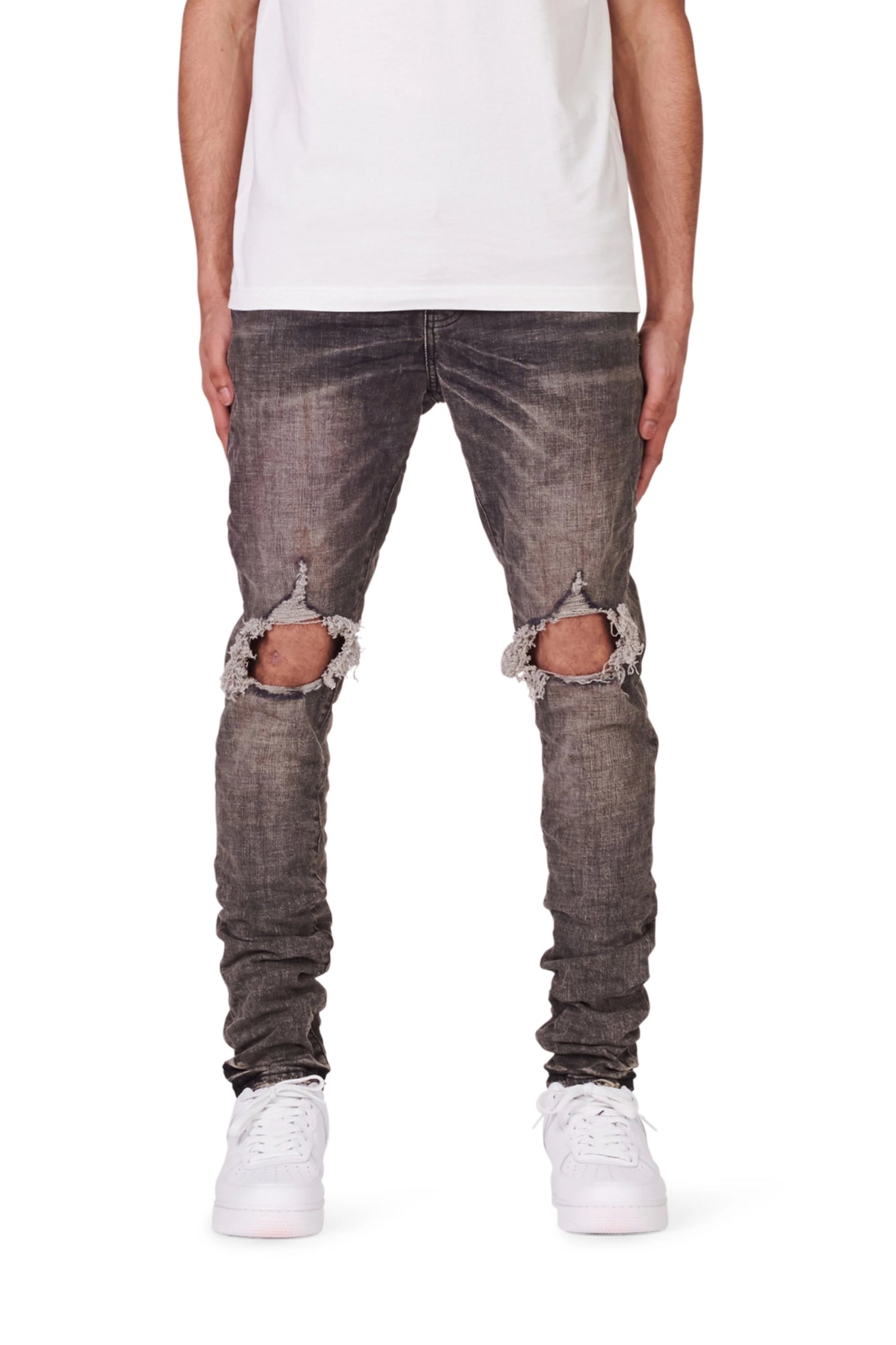 A person wearing a white t-shirt, PURPLE BRAND P002-VWBO Vintage Worn Blowout Black jeans, and white sneakers stands facing forward.