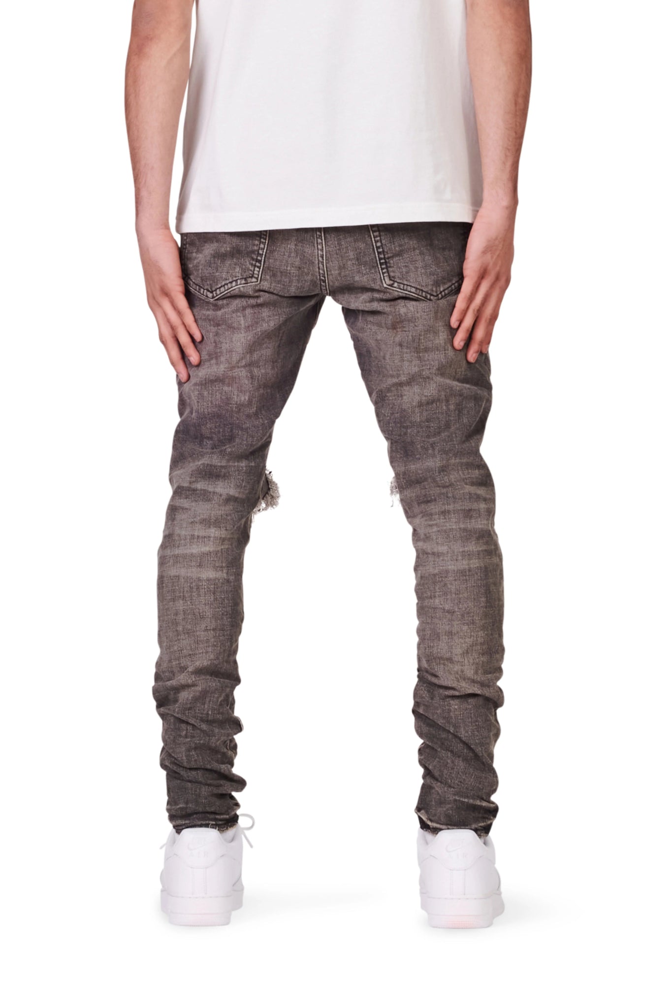 Person shown from the back wearing PURPLE BRAND P002-VWBO Vintage Worn Blowout Black jeans, a white t-shirt, and white sneakers, standing against a plain white background.