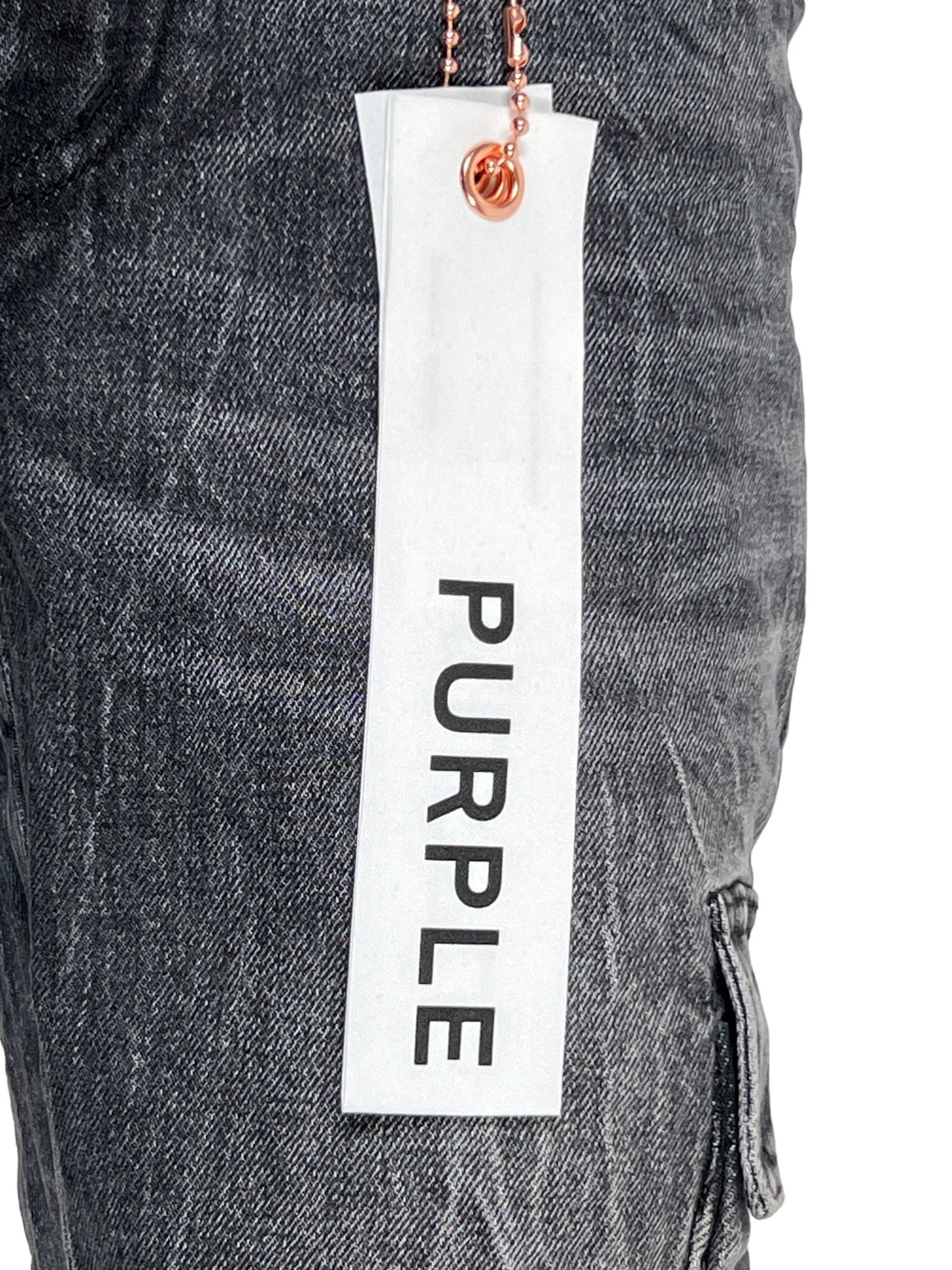 Close-up of a white tag with the word "PURPLE" hanging on the side of a pair of dark gray, tinted worn jeans. The PURPLE BRAND P004-CFTW CARGO FLARE TINTED WORN BLACK jeans, part of the PURPLE BRAND collection, feature a visible side pocket and texture detail.