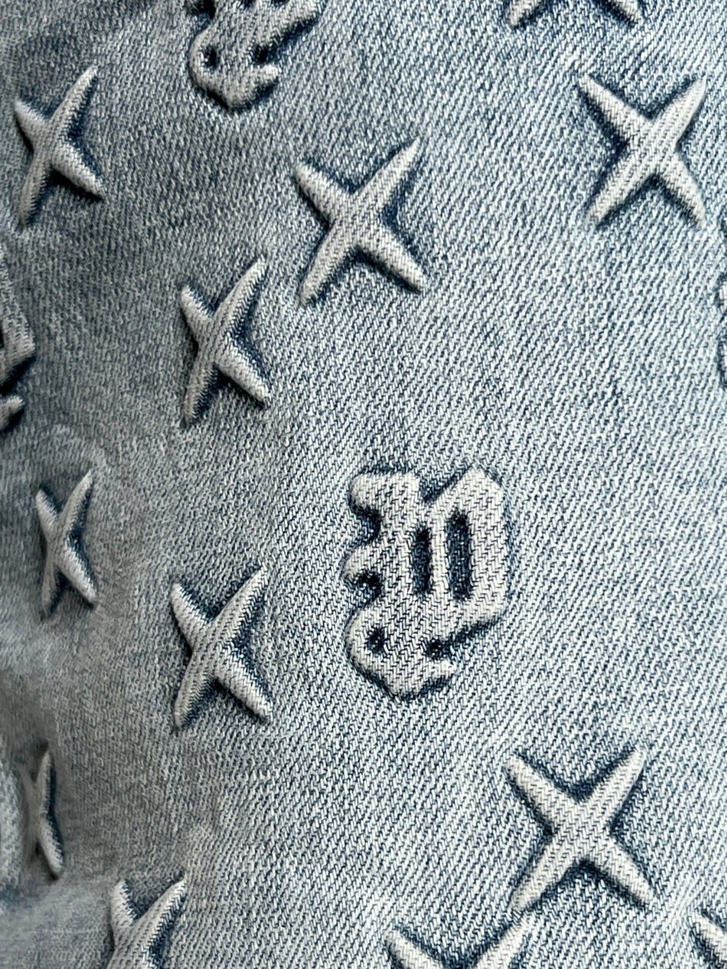 Close-up of indigo denim with embossed X shapes and Gothic "w" details, as seen on the PURPLE BRAND P004-FOBL425 Flare Mono Embossed Indigo jeans.
