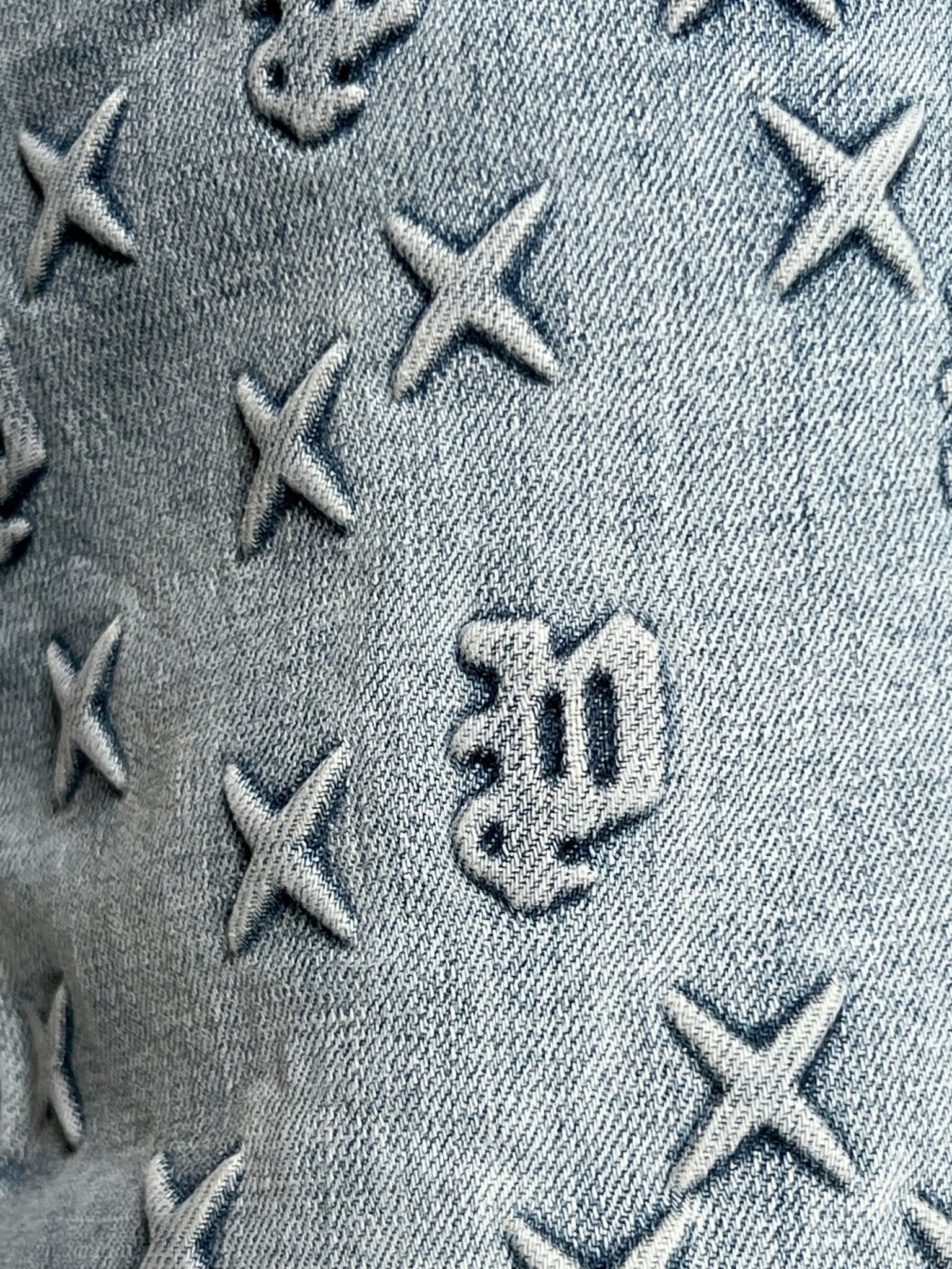 Close-up of indigo denim with embossed X shapes and Gothic "w" details, as seen on the PURPLE BRAND P004-FOBL425 Flare Mono Embossed Indigo jeans.
