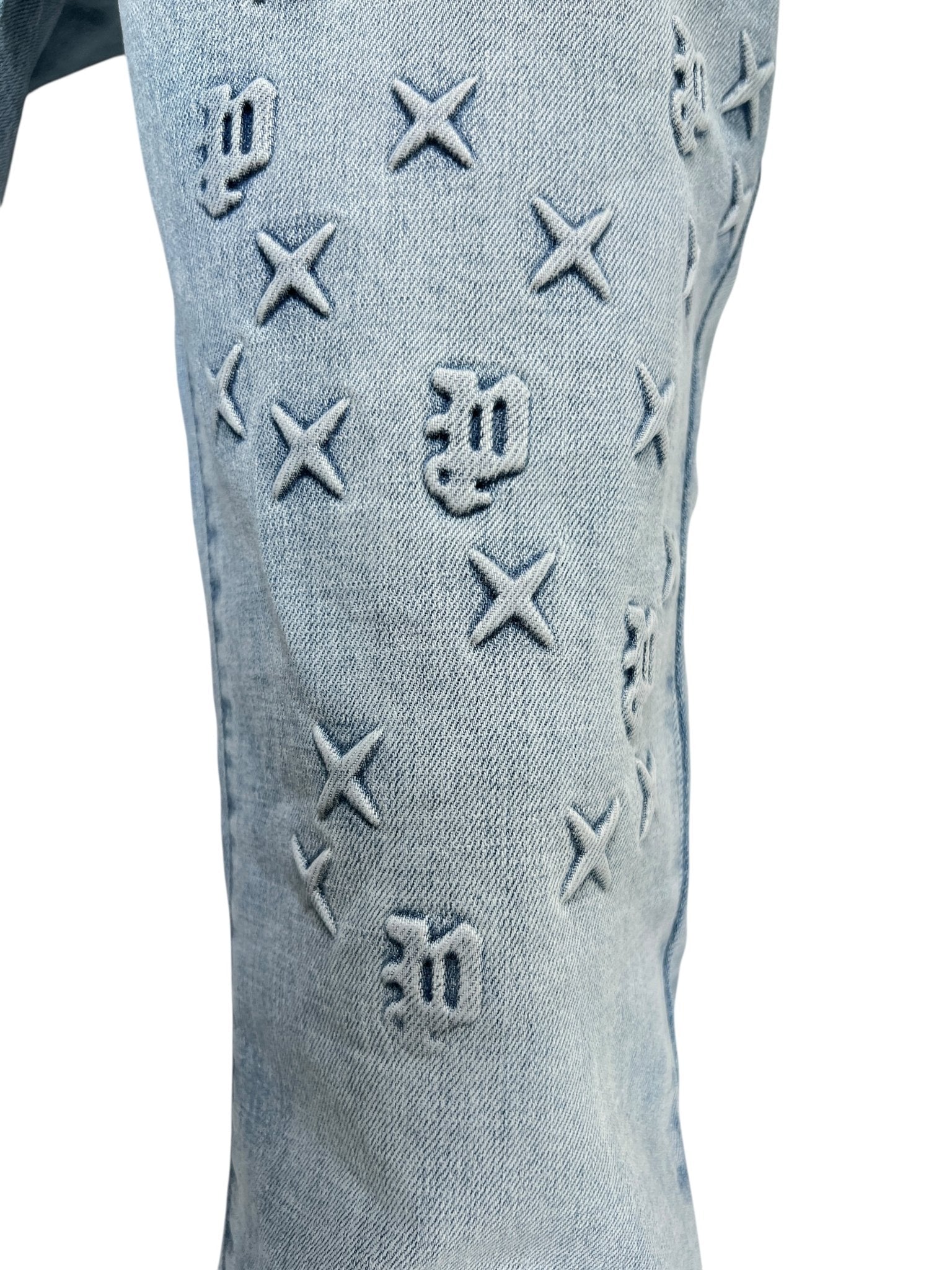 Close-up of PURPLE BRAND P004-FOBL425 Flare Mono Embossed Indigo jeans featuring raised embossed details, including X shapes and stylized letter motifs.