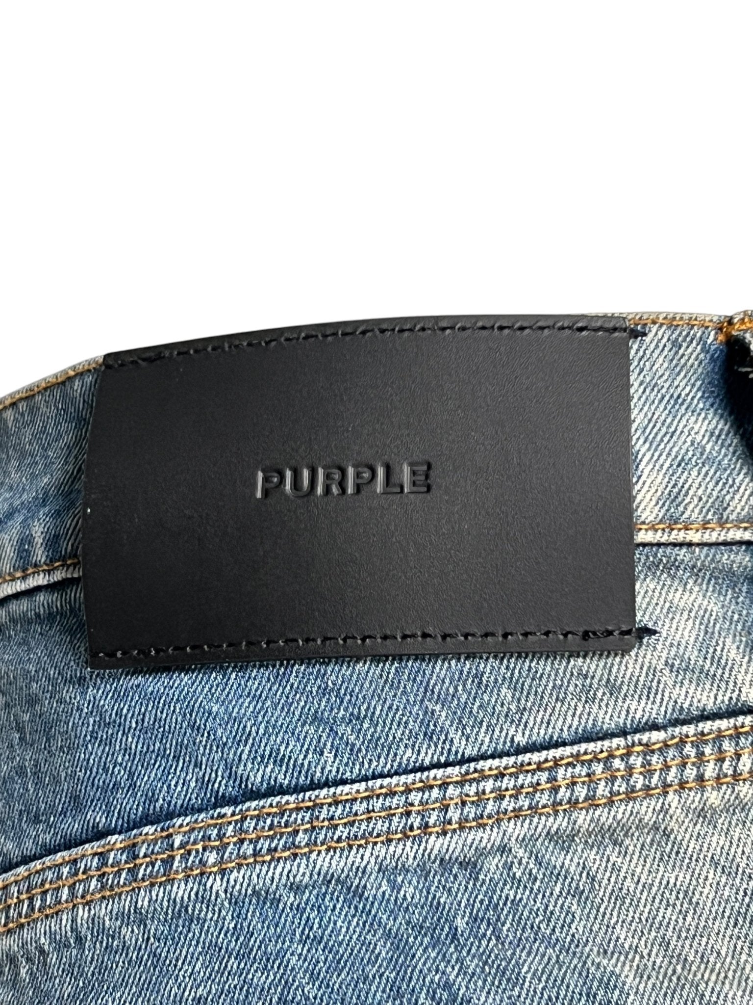Close-up of Purple Brand P004-GBMF Gaia Blowout Flare Indigo Denim jeans with a black leather "PURPLE BRAND" patch on the waistband, showcasing the sophisticated style for Spring/Summer 2025.