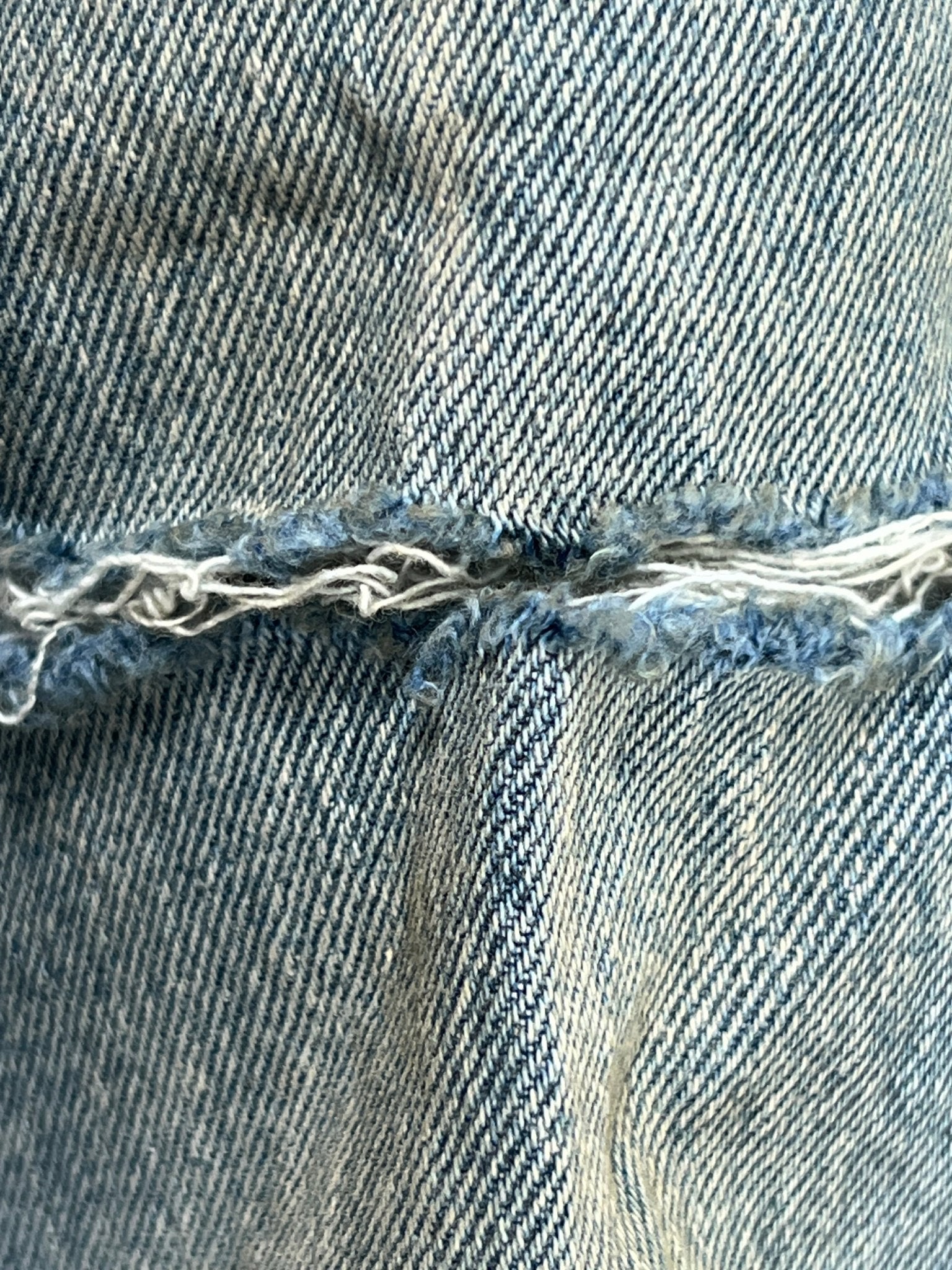 A close-up of a frayed seam on the Purple Brand P004-GBMF Gaia Blowout Flare Indigo Denim offers a sophisticated glimpse into PURPLE BRAND's Spring/Summer 2025 collection, highlighting the wear and texture of the indigo fabric.