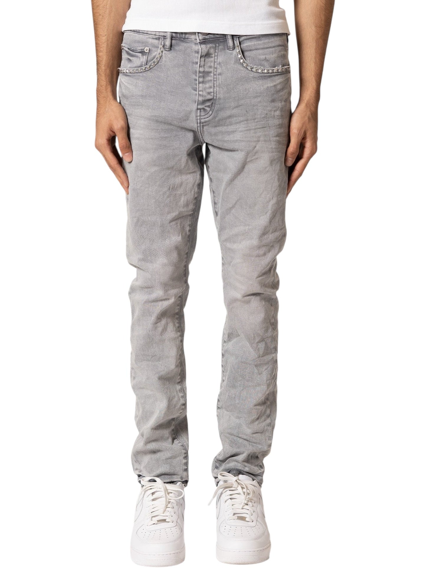 A person wearing PURPLE BRAND Purple Brand P005-AYDG325 Alloy Studs Overdyed Grey men's jeans with a white shirt and white sneakers, shown from the waist down against a plain background.