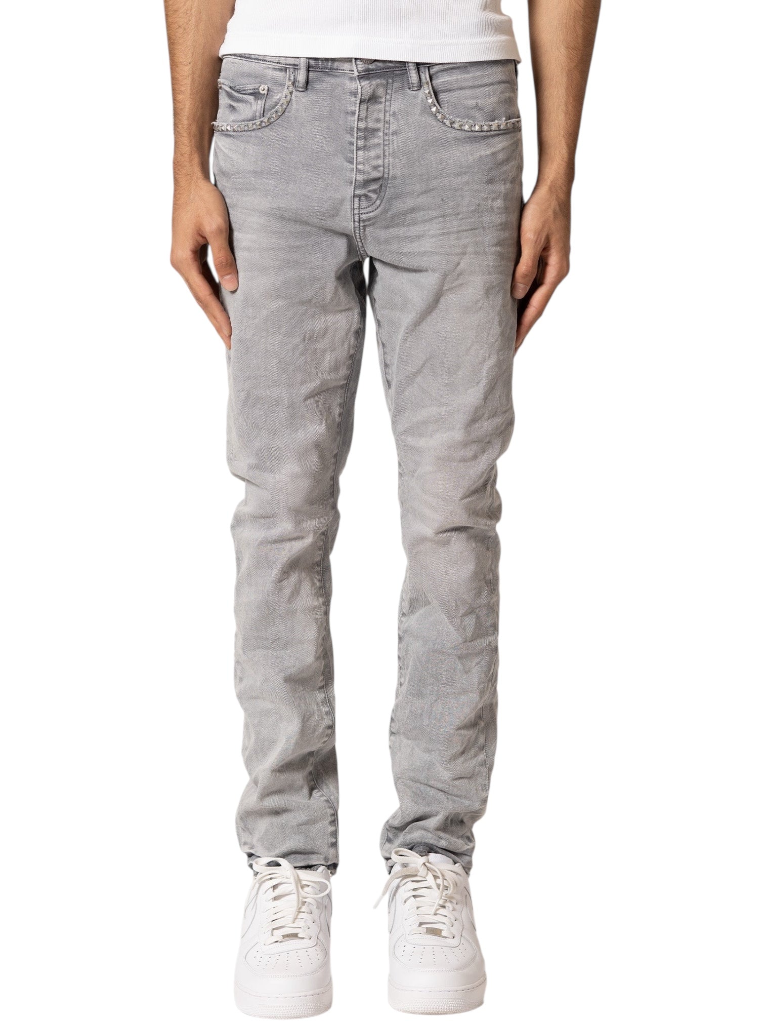 A person wearing PURPLE BRAND Purple Brand P005-AYDG325 Alloy Studs Overdyed Grey men's jeans with a white shirt and white sneakers, shown from the waist down against a plain background.