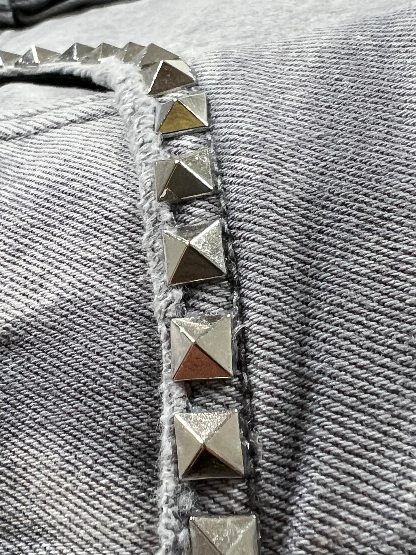 Close-up of metallic pyramid studs in a row on textured gray fabric, featured on PURPLE BRAND's Purple Brand P005-AYDG325 Alloy Studs Overdyed Grey.