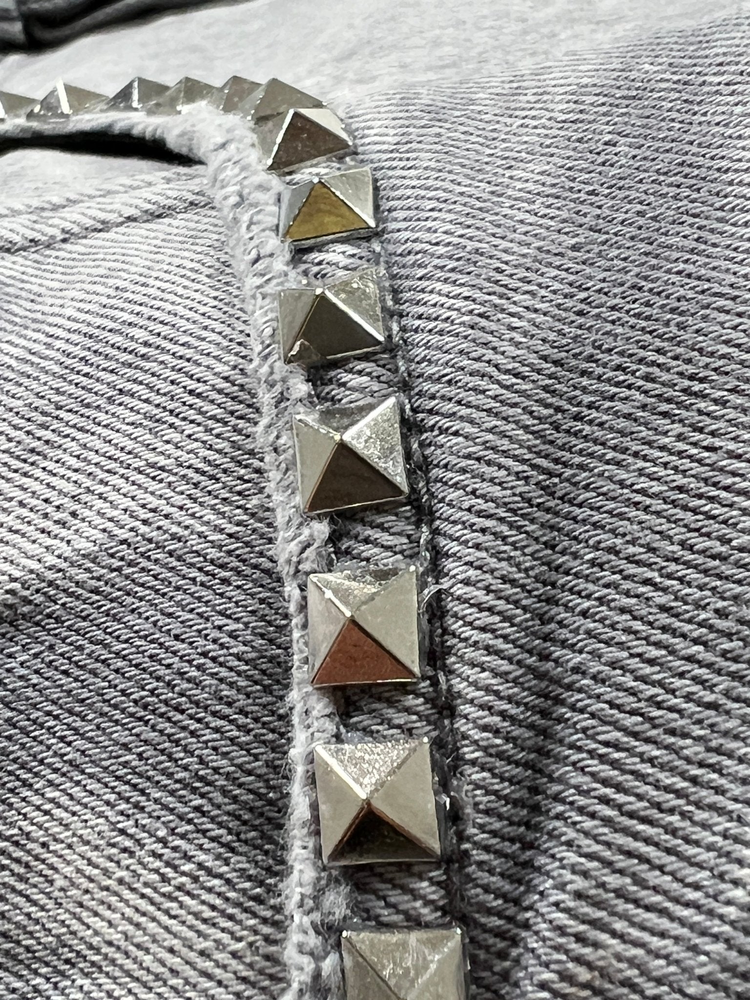 Close-up of metallic pyramid studs in a row on textured gray fabric, featured on PURPLE BRAND's Purple Brand P005-AYDG325 Alloy Studs Overdyed Grey.