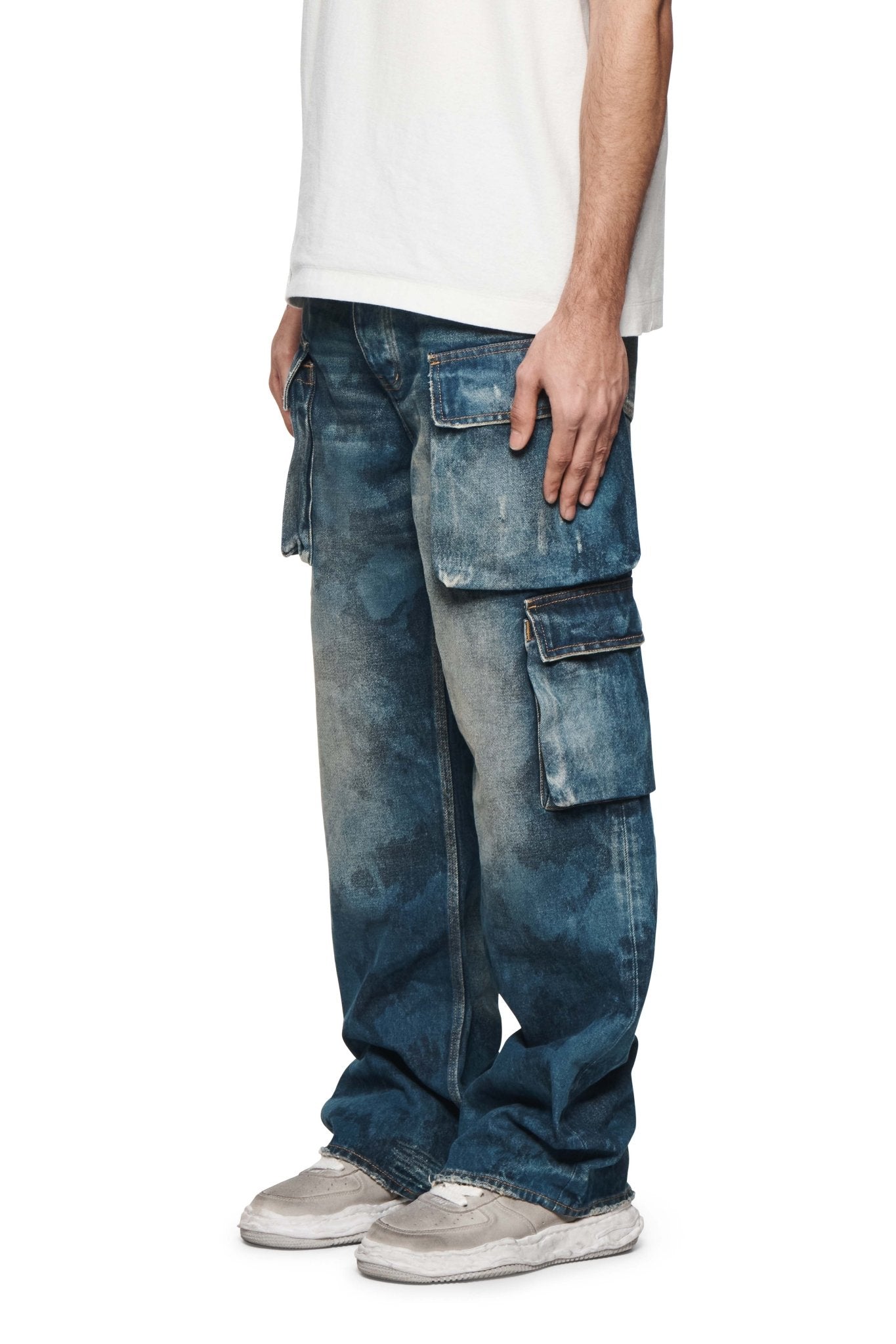 A person is standing wearing PURPLE BRAND P018-TPDI TRIPLE POCKET CARGO DK INDIGO jeans, a white T-shirt, and white sneakers.