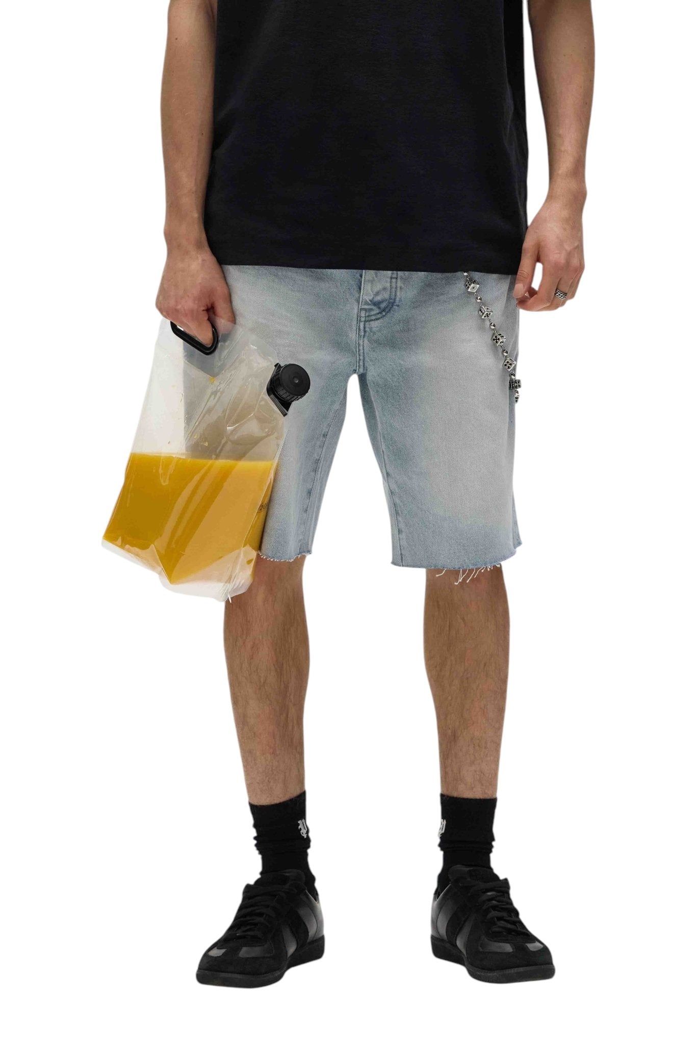 A person in a black shirt and Purple Brand P059-CBLT Ciel Blue Shorts holds a large, transparent bag filled with orange liquid, effortlessly blending casual style with a laid-back vibe.