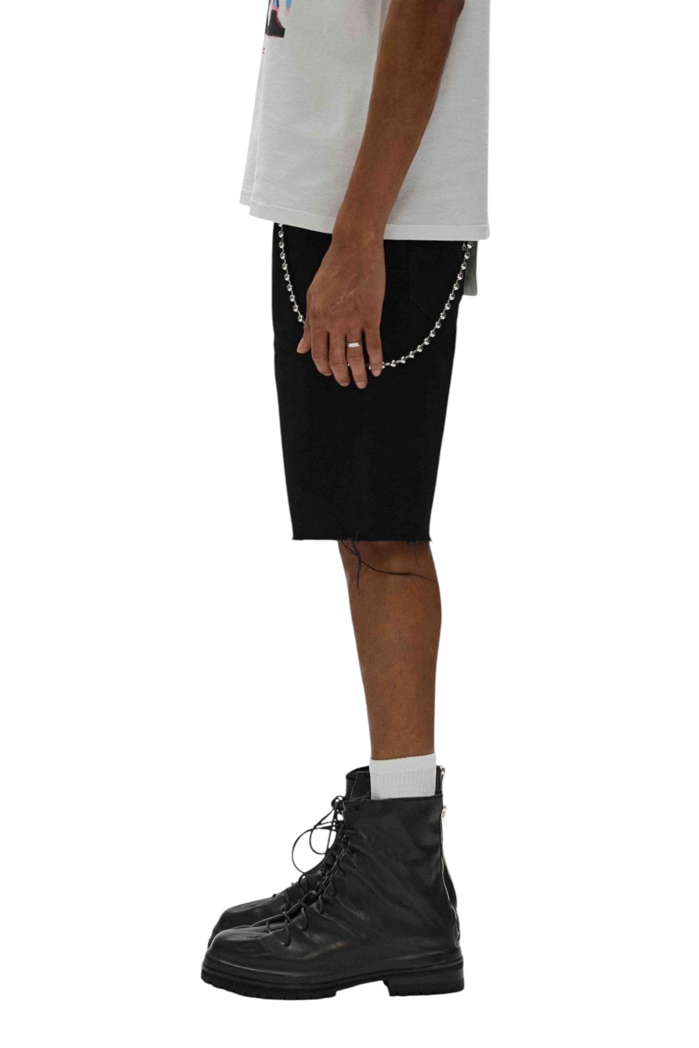 A person in a relaxed-fit white shirt and Purple Brand P059-MDSB Midnight Shorts Blk, accessorized with a chain, is wearing black lace-up boots and standing in profile.