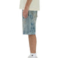 A person standing sideways wears a textured white shirt, PURPLE BRAND P059-MXPS Mixed Paint Shorts Indigo, white crew socks, and white sneakers against a white background.