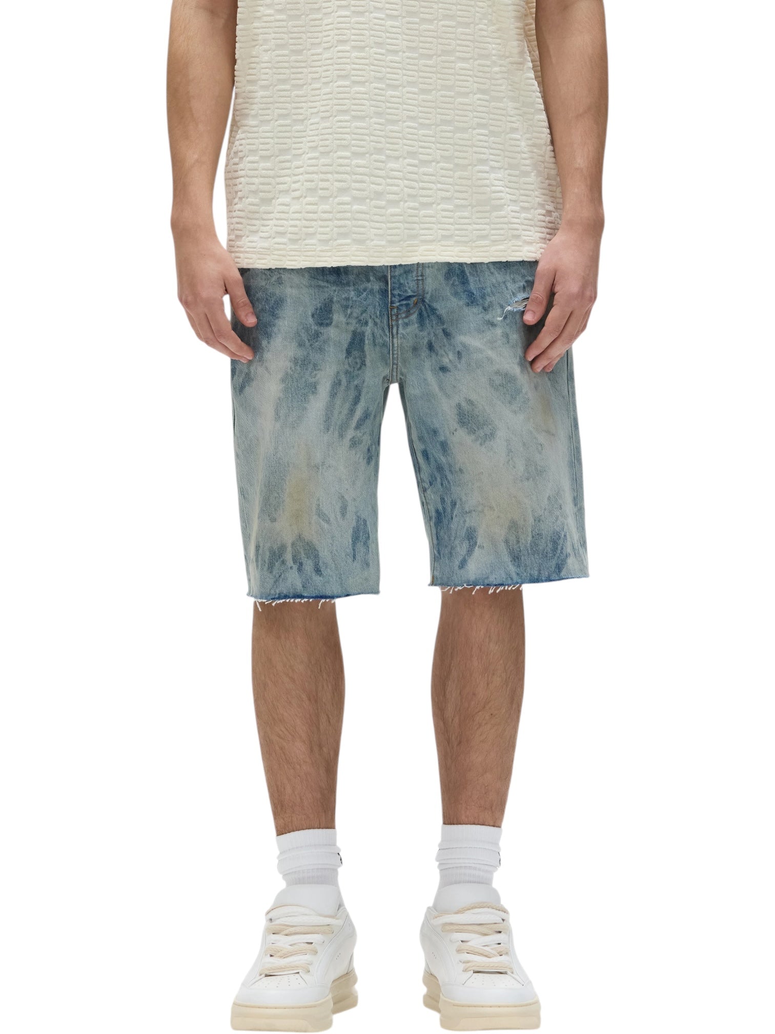 Wearing a textured cream t-shirt, relaxed fit, PURPLE BRAND Purple Brand P059-MXPS Mixed Paint Shorts Indigo, white socks, and white sneakers, a person stands against a plain background.