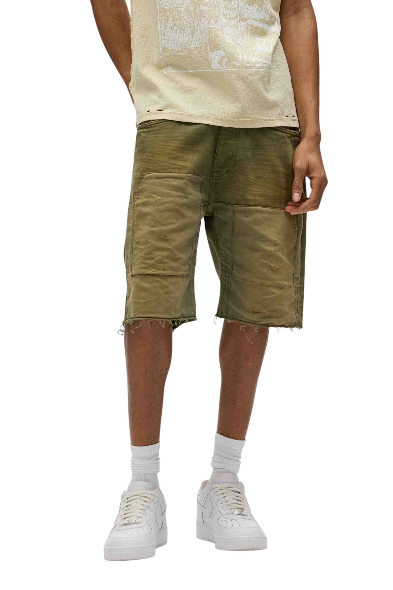 Someone is wearing a beige t-shirt, the Purple Brand P059-PGSO Patchwork Short Overdye Grn relaxed fit cargo shorts with 5 pockets, white socks, and white sneakers against a white background.