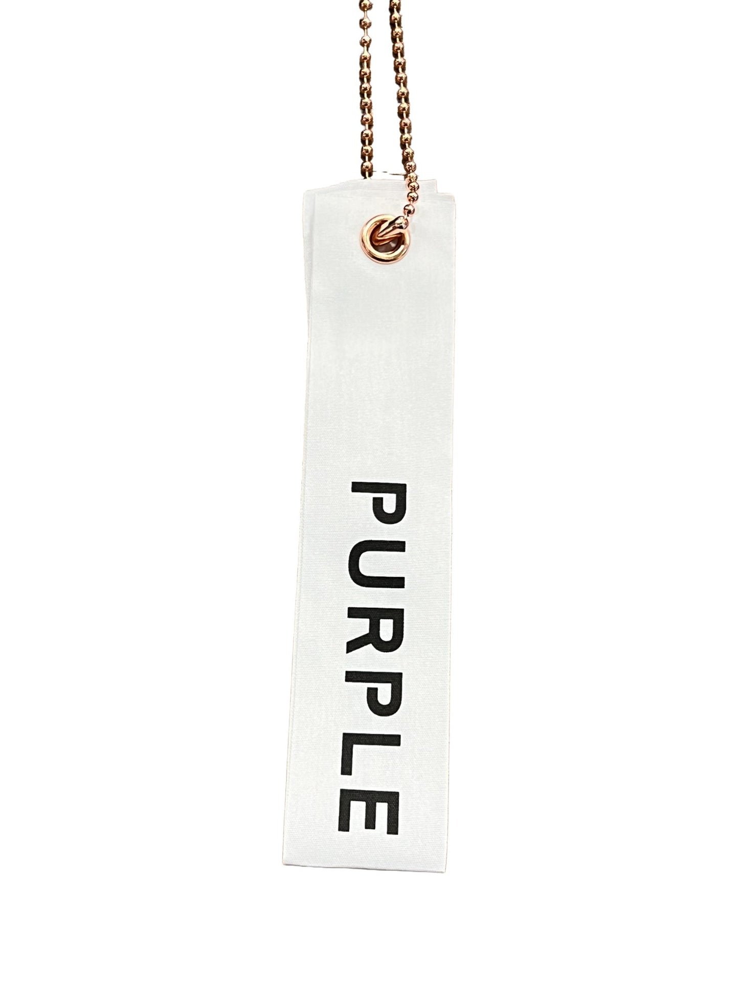 A WHITE TEXTURED JERSEY LABEL WITH THE WORD "PURPLE" PRINTED IN BLACK, HANGING FROM A BRONZE CHAIN.