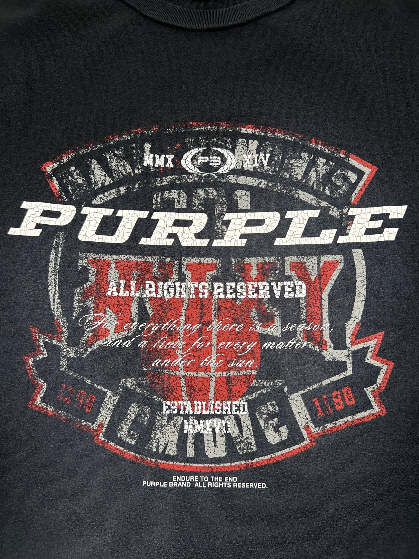 The PURPLE BRAND P101-JWBS TEXTURED INSIDE OUT TEE BLACK features a distressed, circular graphic with bold white "PURPLE" text and red accents, surrounded by smaller white and red text and numbers. Perfect for fans of PURPLE BRAND.