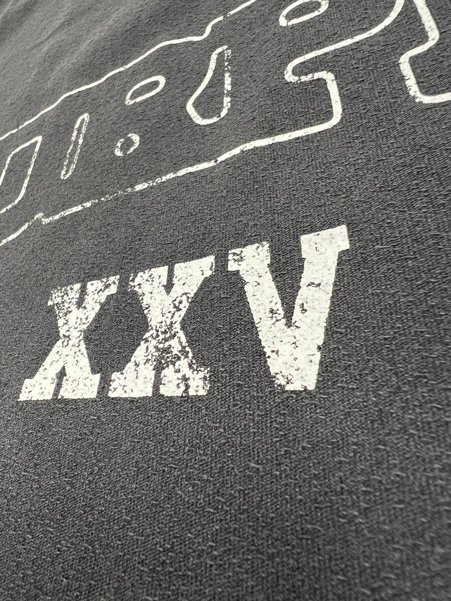 A close-up of the PURPLE BRAND P101-TBSO425 Textured Inside Out Tee Blk, crafted from 100% cotton, shows its dark textured fabric with faded white "XXV" Roman numerals printed on it.