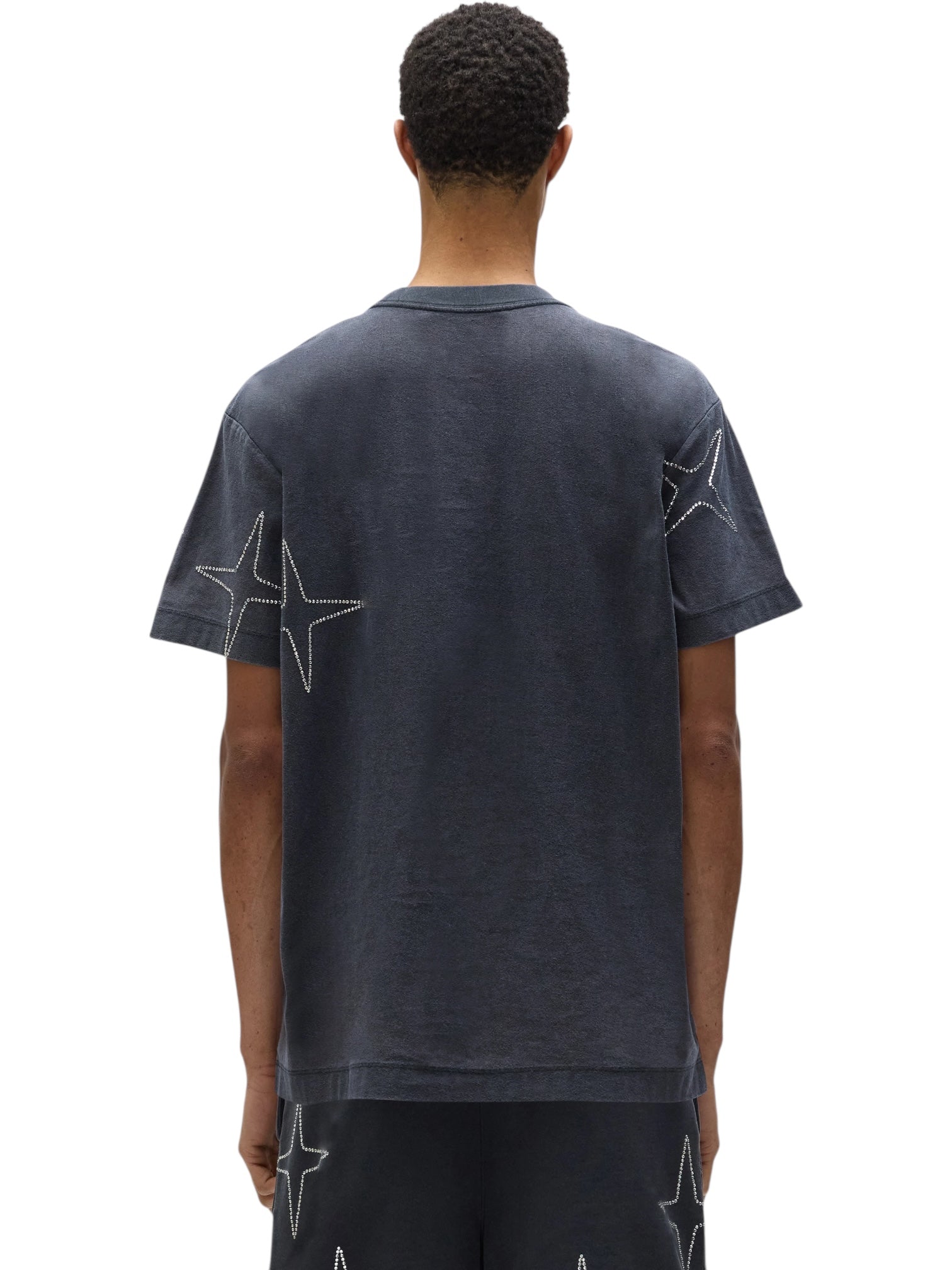 A person is shown from the back wearing a PURPLE BRAND P104-TBCS325-Textured SS Tee Black Beauty, featuring star-shaped stitched designs on the sleeves and upper back, paired with matching dark shorts.