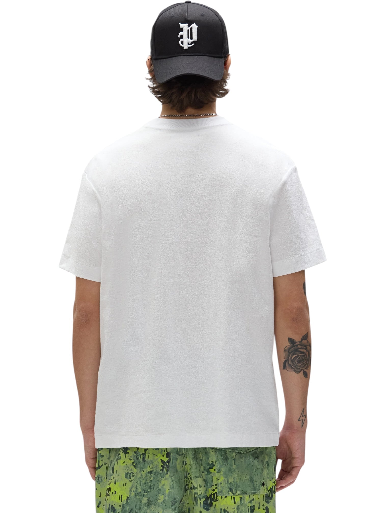 A person wears the PURPLE BRAND P104-TWGC325 Textured Jersey SS Tee in white, paired with camo shorts and a black cap with a white "P," revealing a rose tattoo on their left forearm. The 100% cotton tee looks both comfortable and stylish.