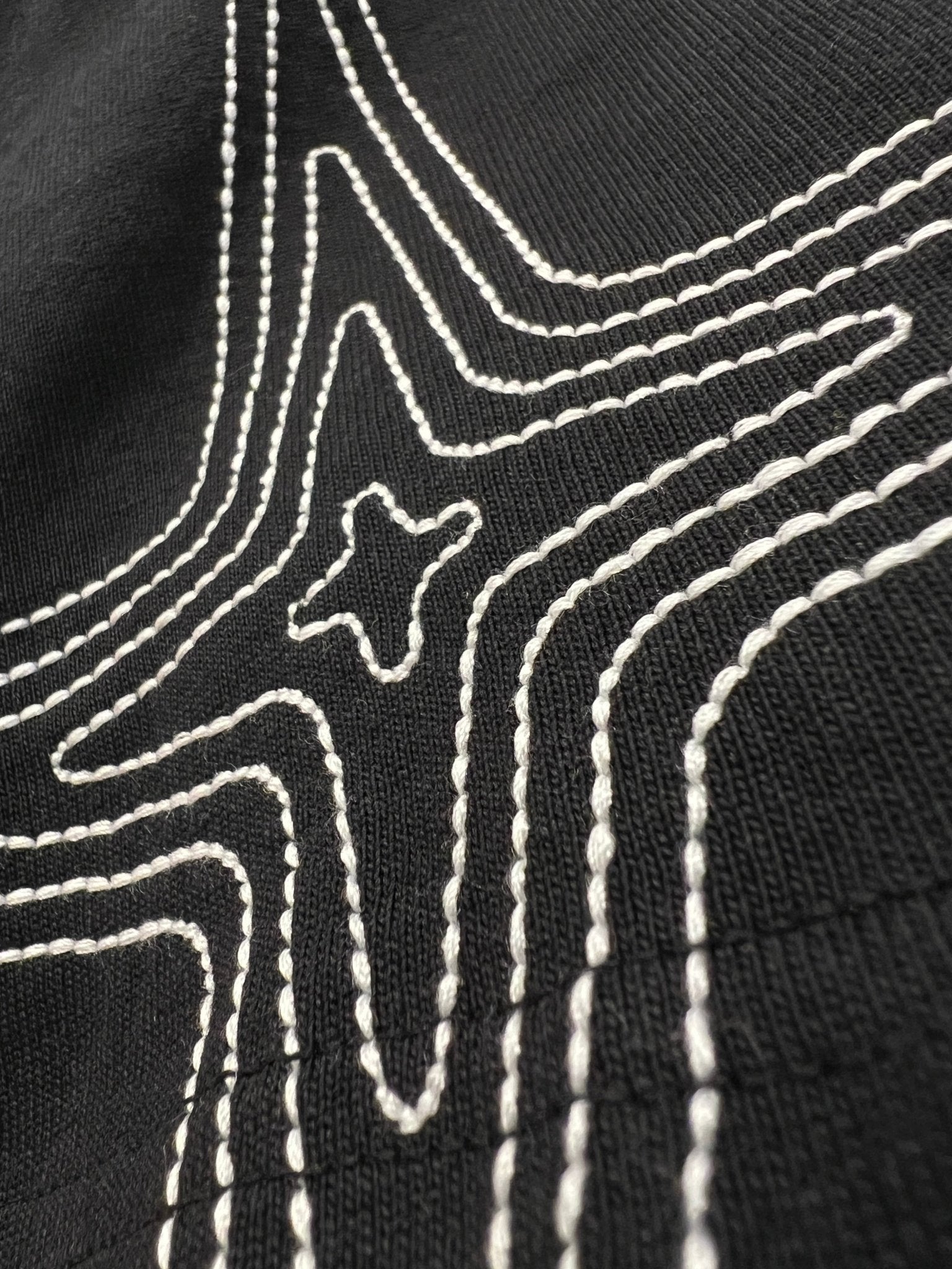 Close-up of the PURPLE BRAND P117-HBJS325 HWT Jersey SS Tee in Black, featuring distinctive white stitched lines forming a bold geometric star pattern on the graphic t-shirt.
