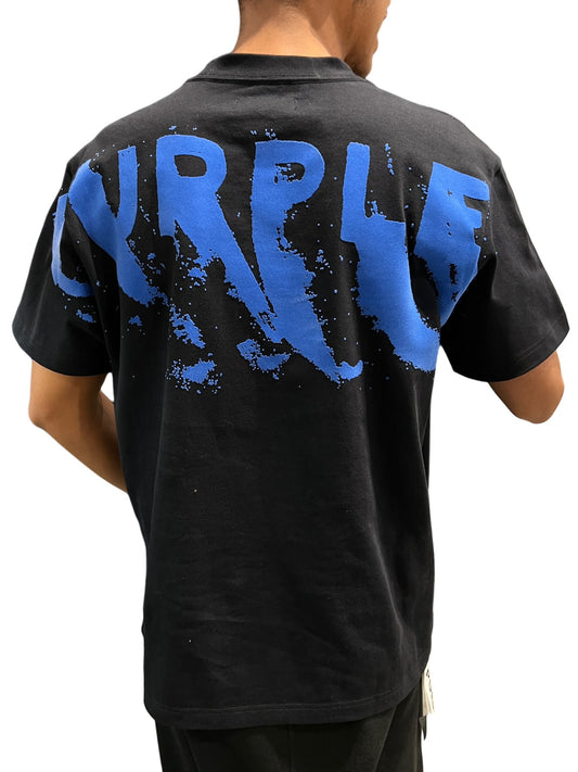 A person from behind is wearing a black 100% cotton PURPLE BRAND PURPLE BRAND P117-HJBW823 HWT JERSEY TEE BLACK graphic t-shirt with the word "purple" printed in large blue letters.