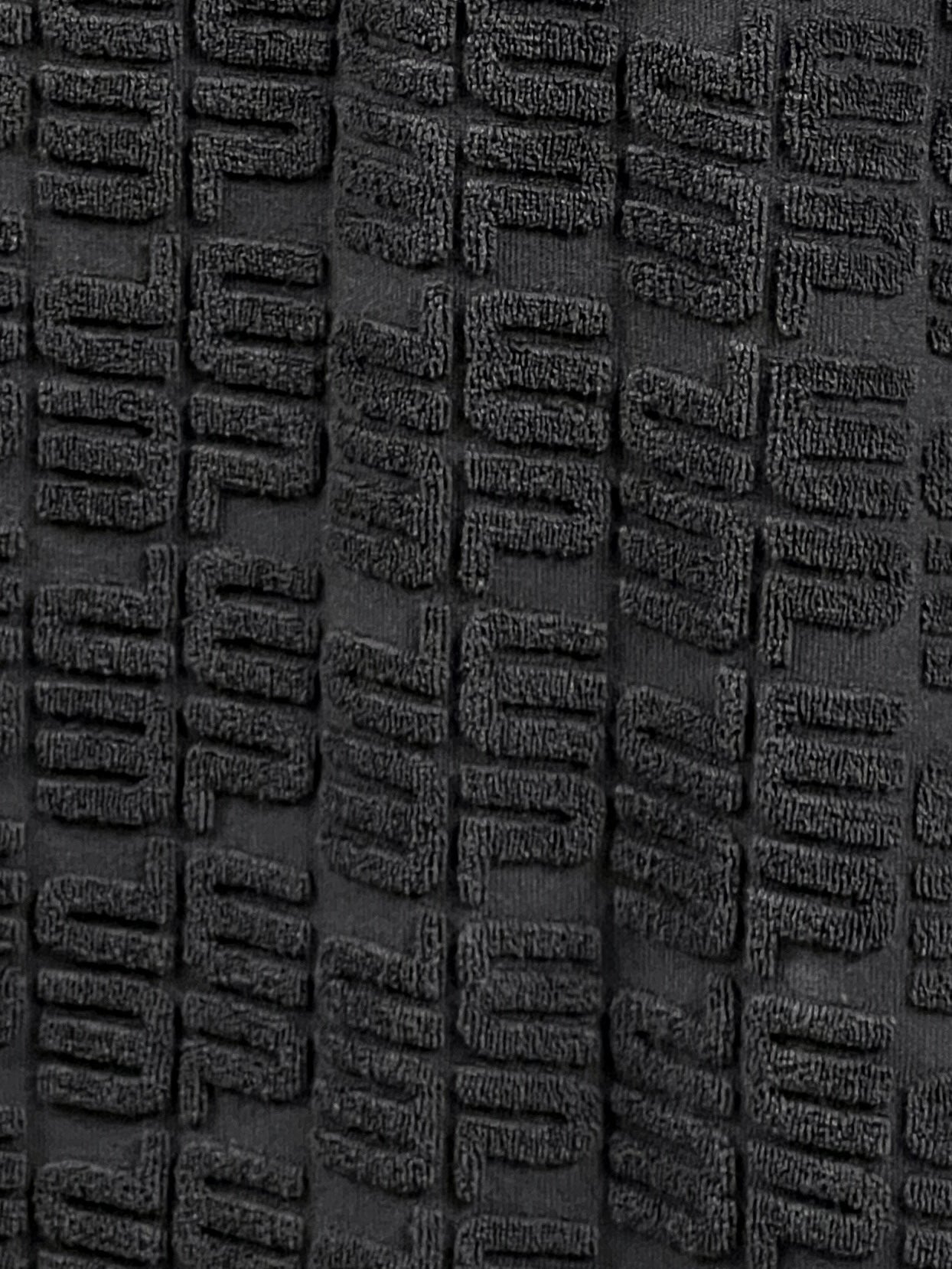 Close-up of a textured dark gray fabric with a raised, rectangular pattern arranged in a repetitive, grid-like design, reminiscent of the intricate detailing found in the PURPLE BRAND P138-JTBB TERRY TOWEL POLO BLACK from PURPLE BRAND's Pre Fall 2024 collection.