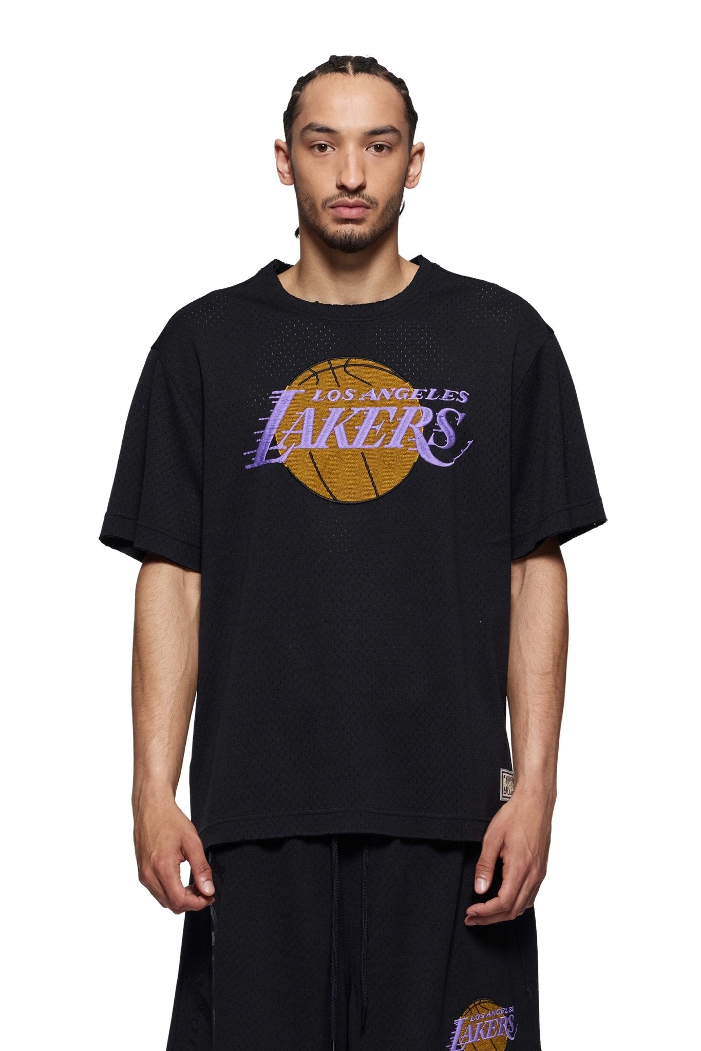 A man with braided hair proudly wears a Purple Brand P142-MNLA824 LA Lakers Mesh Tee Black, highlighting his status as a dedicated NBA fan.