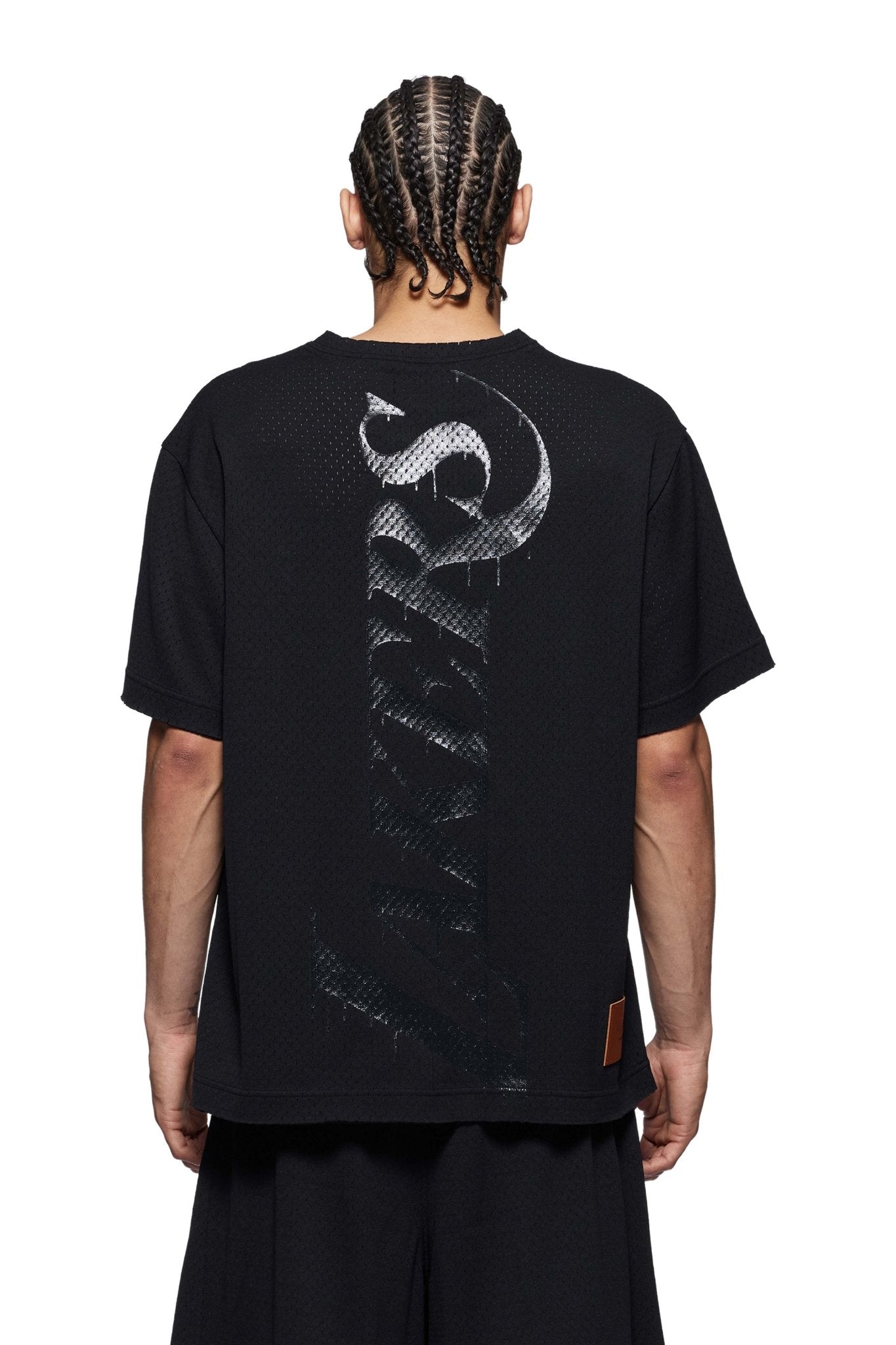 A person with braided hair wears a Purple Brand P142-MNLA824 LA Lakers Mesh Tee in black, proudly displaying their NBA fandom with "Lakers" stylishly emblazoned on the back.