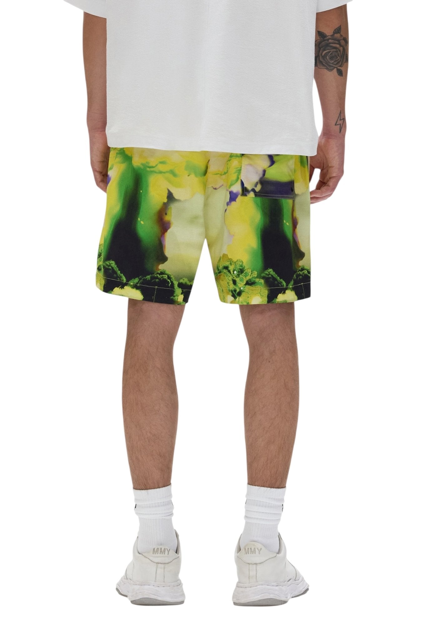 A person wearing a white shirt, PURPLE BRAND P504-PMFM325-All Round Shorts Yellow, white socks, and white sneakers stands with their back to the camera.