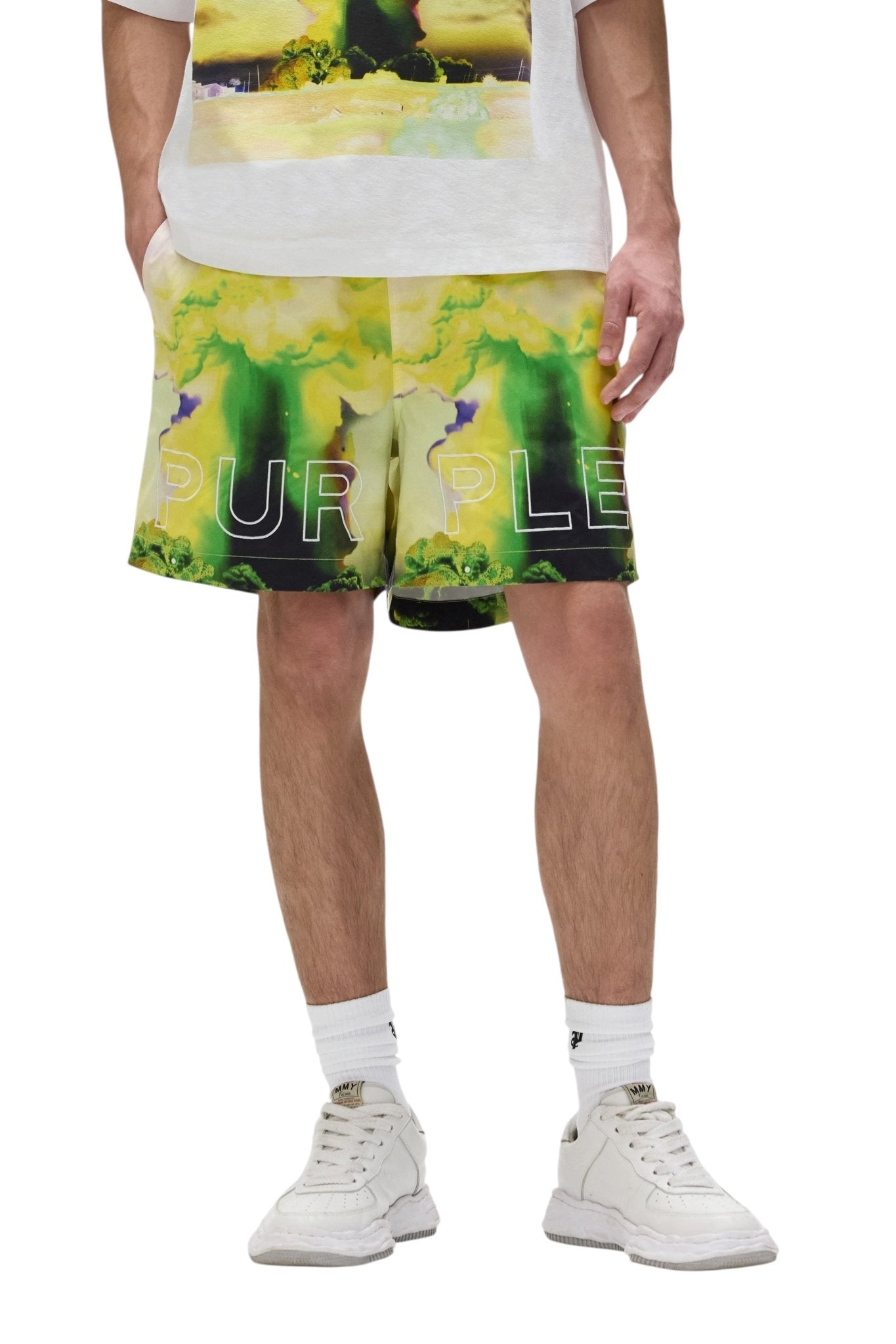 A person wearing white sneakers, white socks, and PURPLE BRAND P504-PMFM325-All Round Shorts Yellow with "PURPLE" printed across the front.