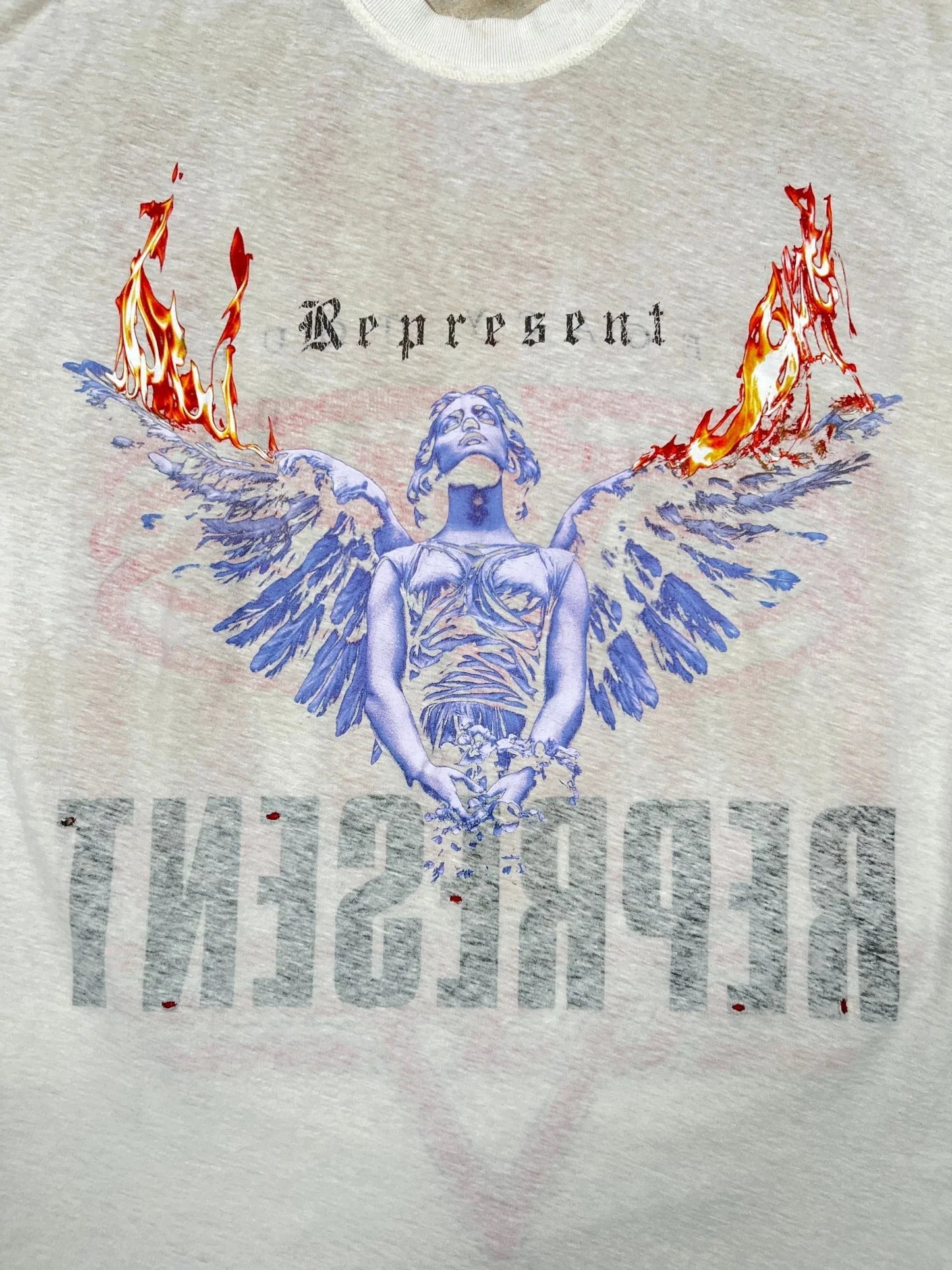 Graphic of a blue-toned angel with fiery wings, "Represent" above and mirrored below, features on the REPRESENT MLM100176-30 Living Legacy T-shirt in Washed Ecru—crafted from premium organic cotton for comfort.