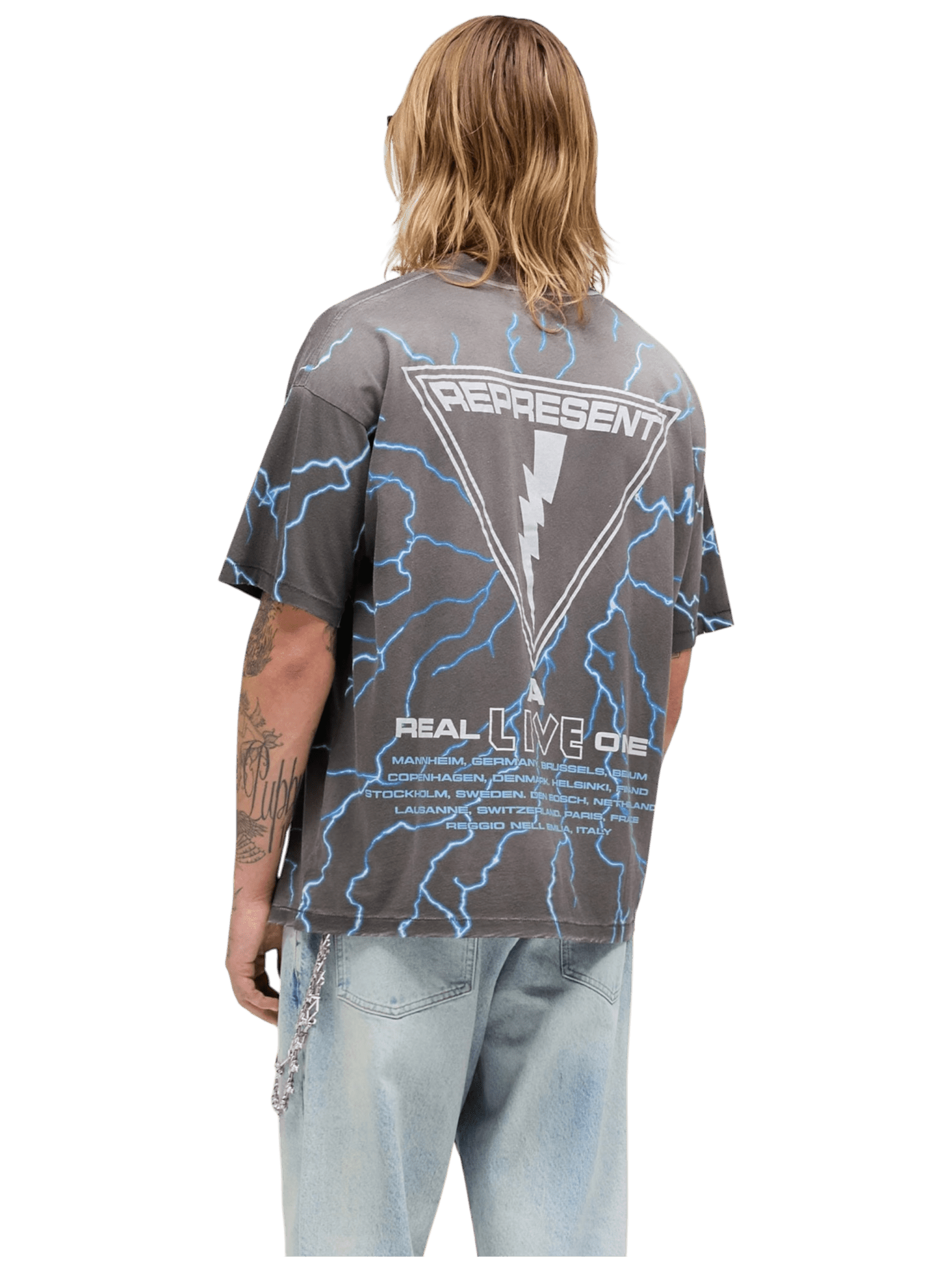 A person with shoulder-length hair and arm tattoos wears the REPRESENT MLM100587-46 Iron Maiden A Real Live One Sunfade Grey tee featuring blue lightning graphics and back text, styled with light blue jeans.