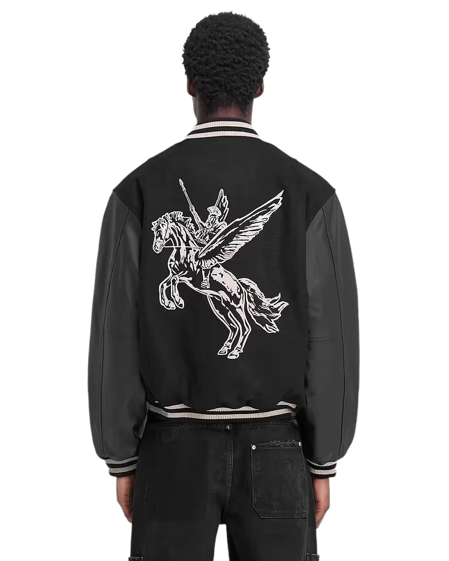 A person wears the REPRESENT MLM1127 Bellerophon Wool Varsity Jacket in black, featuring RiRi zippers and a striking white graphic of a winged horse and rider on the back.