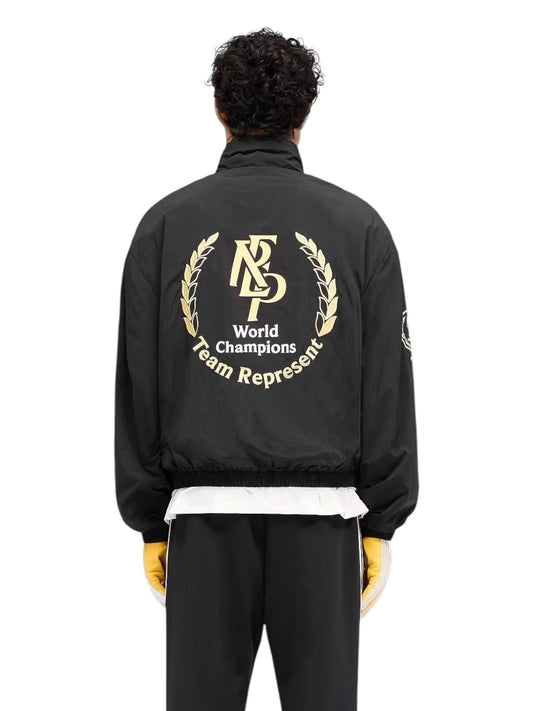 Person wearing a sleek Represent MLM1795 World Championship Jacket in black featuring "World Champions Team Represent" and a laurel design on the back, paired with striking yellow gloves and black pants.