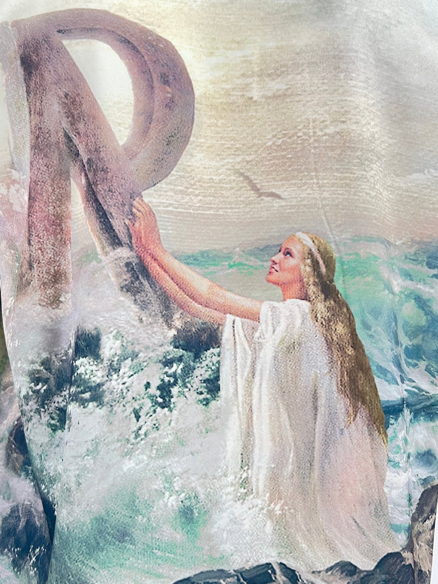 A woman in a white dress stands in the ocean, touching a large, weathered letter "R" amidst waves and seagulls, capturing the essence of a REPRESENT REPRESENT MLM206-137 HIGHER TRUTH PRINTED SHIRT MULT.