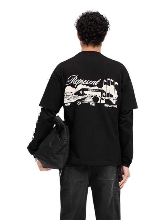 A person wearing a Represent MLM41063 Raceway Tee in Jet Black with a puff print graphic on the back holds a sleek black bag.