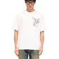 A person wearing glasses and the REPRESENT MLM41066 Elegance in Motion Tee in white, crafted from soft jersey cotton with a winged horse graphic, stands stylishly against a plain background, complemented by classic blue jeans.