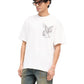 Someone in sunglasses, an oversized Represent MLM41066 Elegance in Motion Tee in White by REPRESENT, made of jersey cotton with a Pegasus design, paired with blue jeans featuring pocket detail, stands against a plain background.