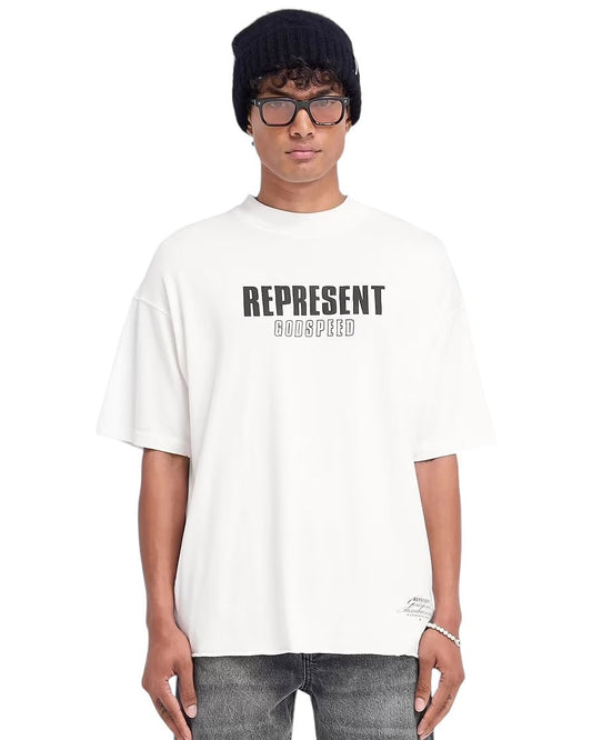 A person wearing a black beanie and glasses sports an oversized "Represent MLM4222 Godspeed T-shirt Flat White" from REPRESENT, which showcases a cracked graphic. They pair it with gray jeans, all set against a white background.