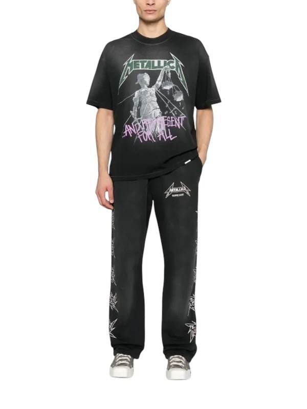 A fashion-forward individual sports the Represent MLM4352 Metallica Justice Tee Blk, styled with band logo pants, standing confidently against a plain white background.